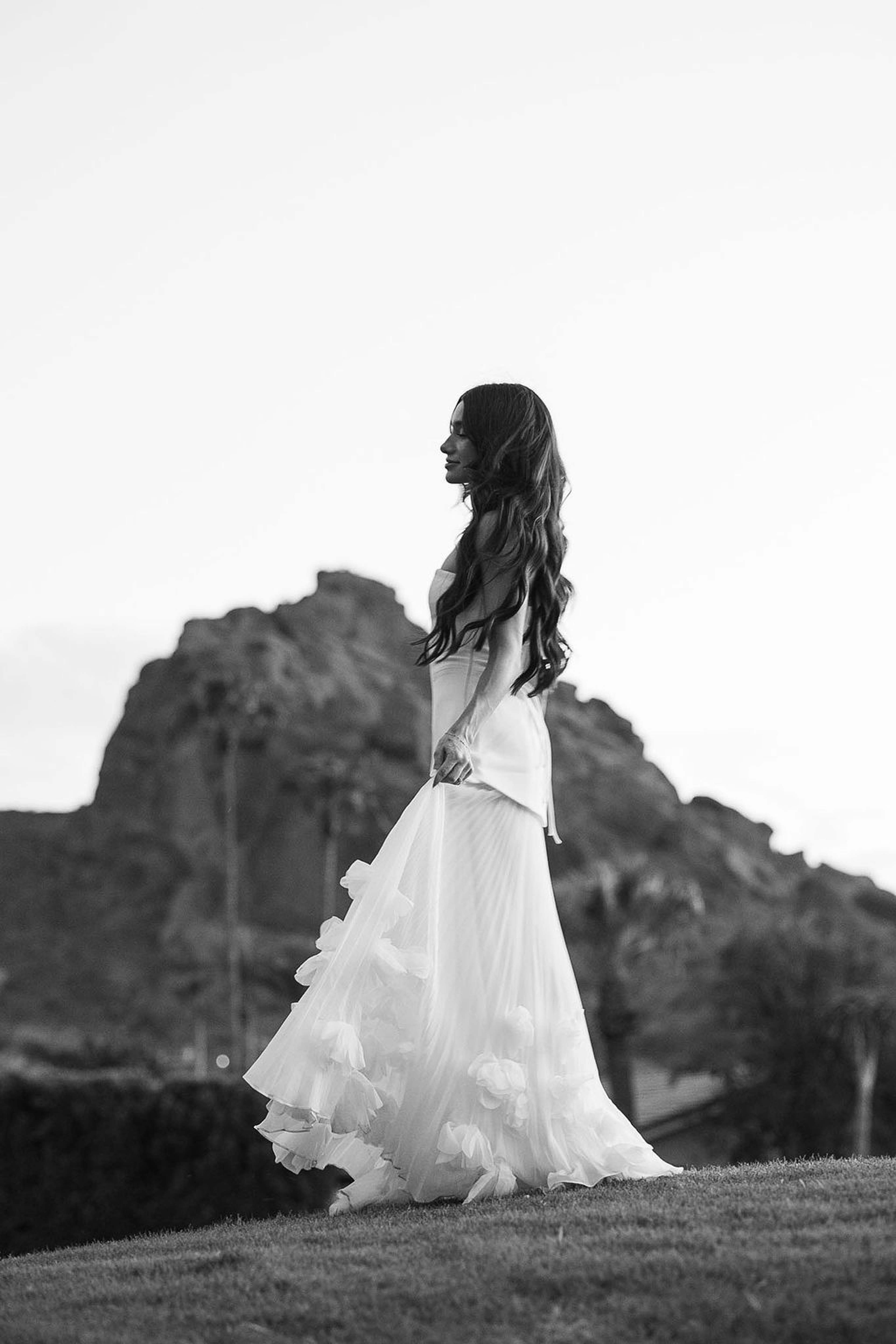 Black and white frame of a woman's gown trailing across grass with the silhouette of Camelback Mountain behind