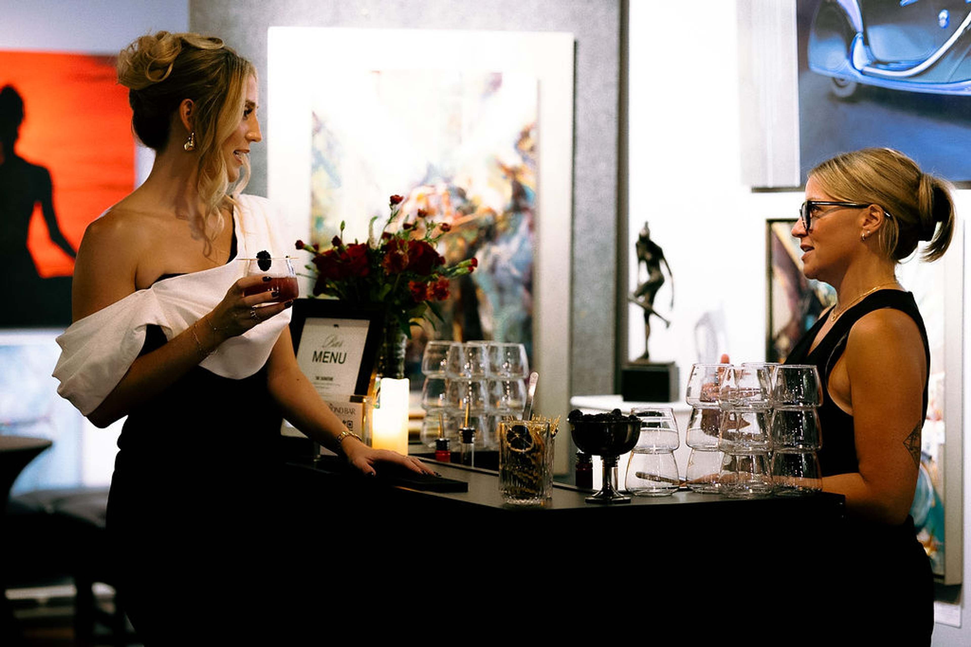Two guests talking across the bar beside the drinks menu