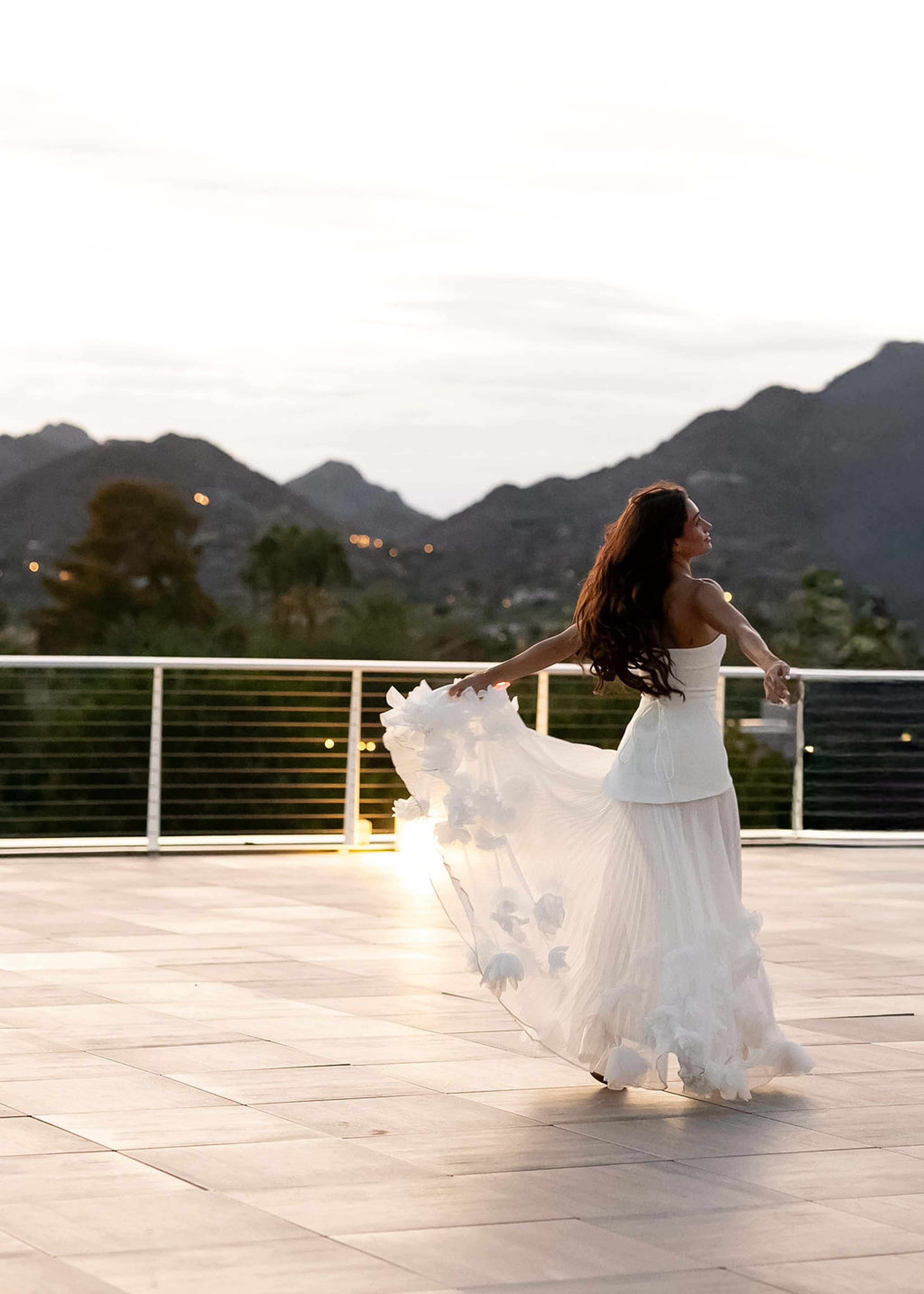 A woman spins on a stone terrace at dusk, her skirt opening into a circle of light