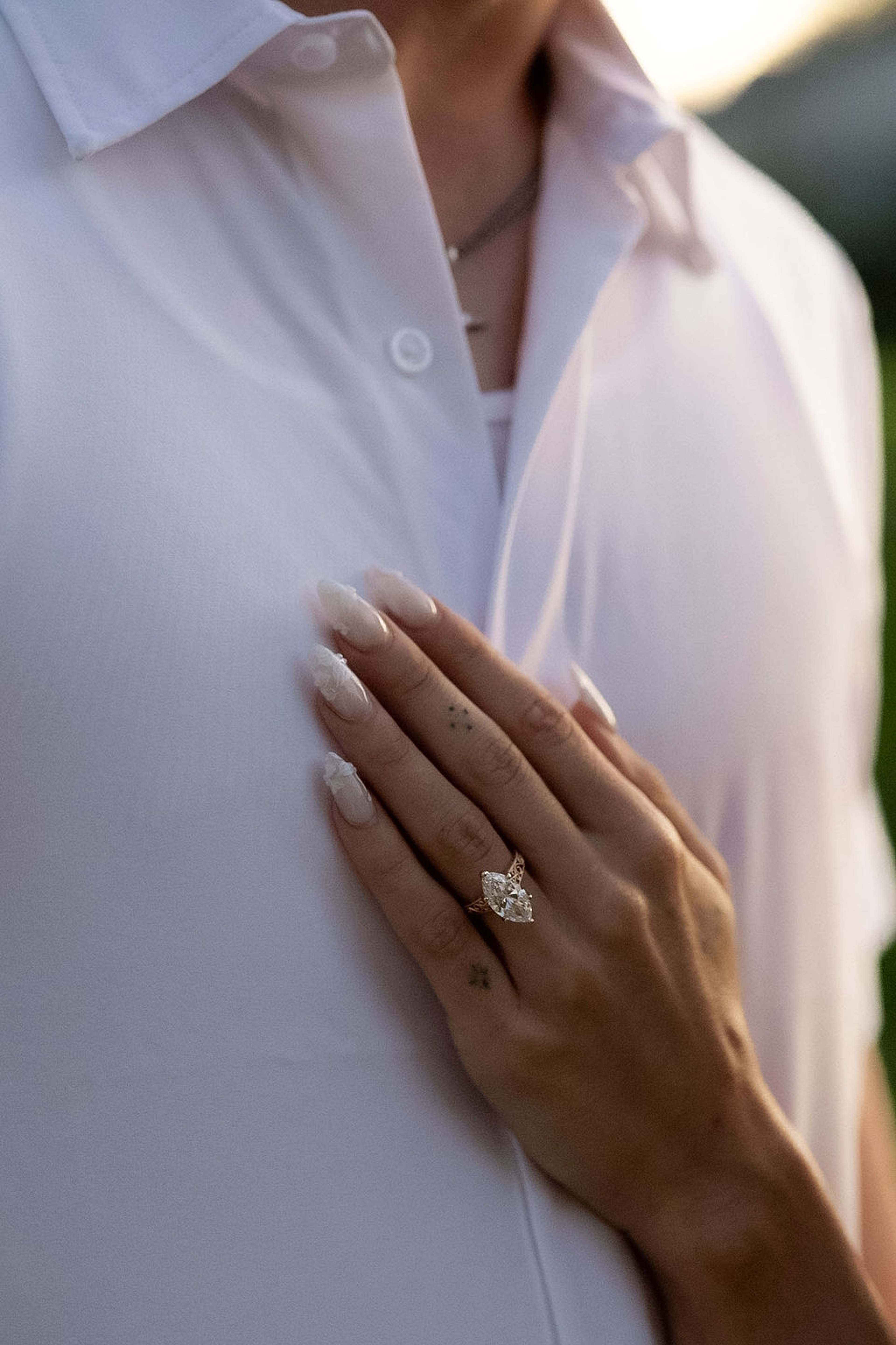 Close detail of a hand with an emerald-cut ring resting against a soft white collar