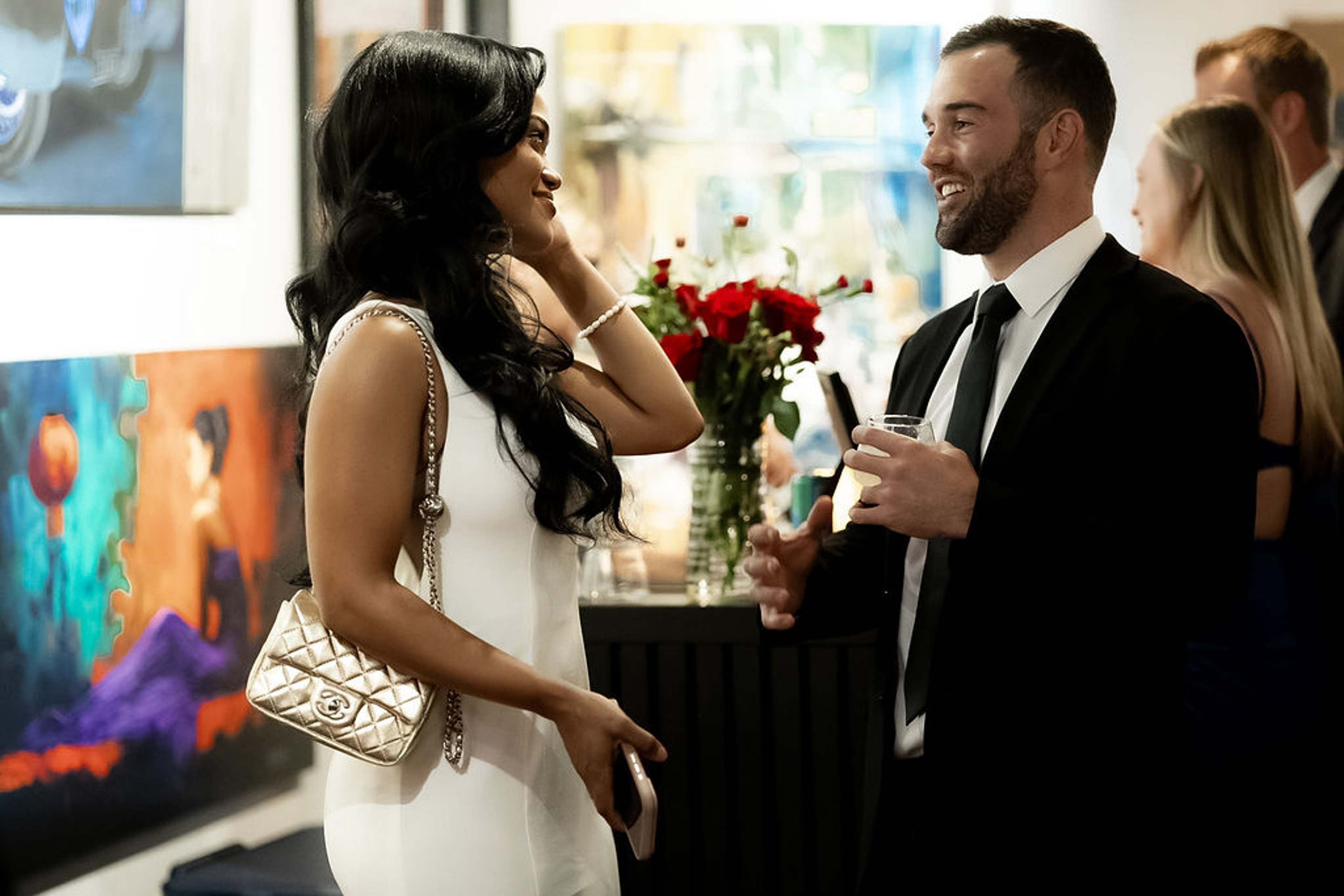 Guest in a white dress in conversation beside a cocktail table of red roses