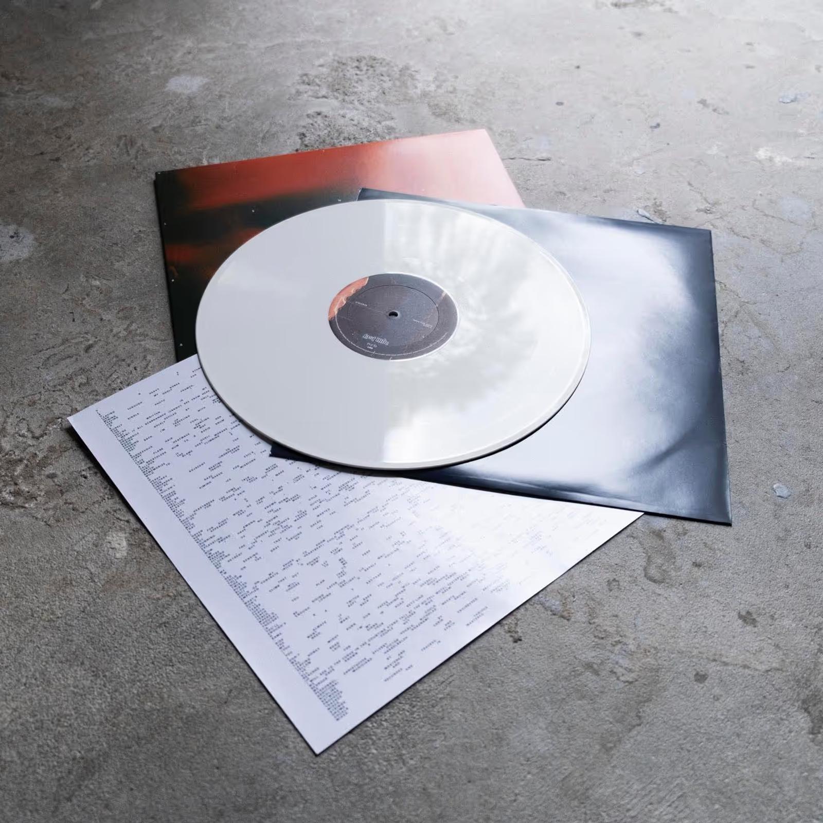 White vinyl record partially placed on two album covers and a printed lyric sheet on a concrete surface.