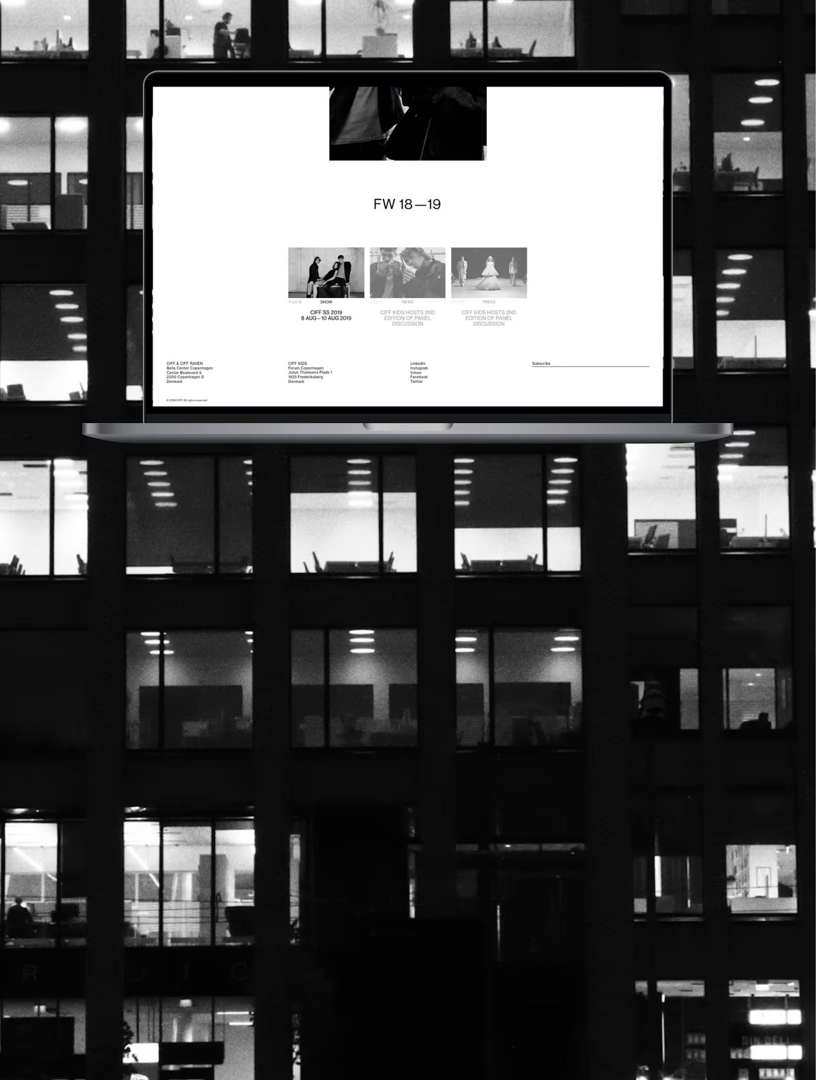 Black and white photo of an office building at night with a floating laptop screen displaying a fashion website for FW 18-19.
