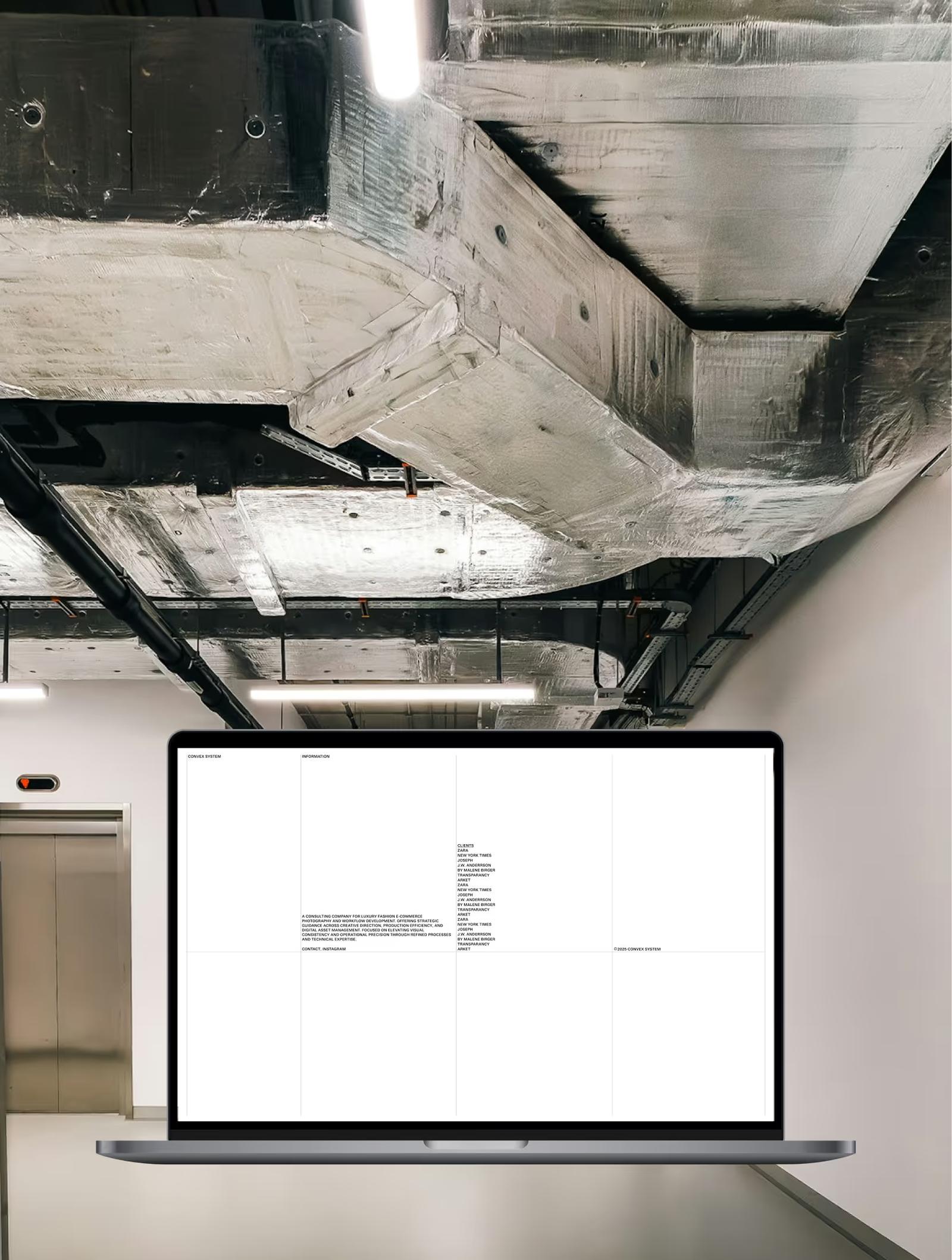 Laptop displaying a webpage with black text on white background, set against an industrial ceiling and elevator backdrop.