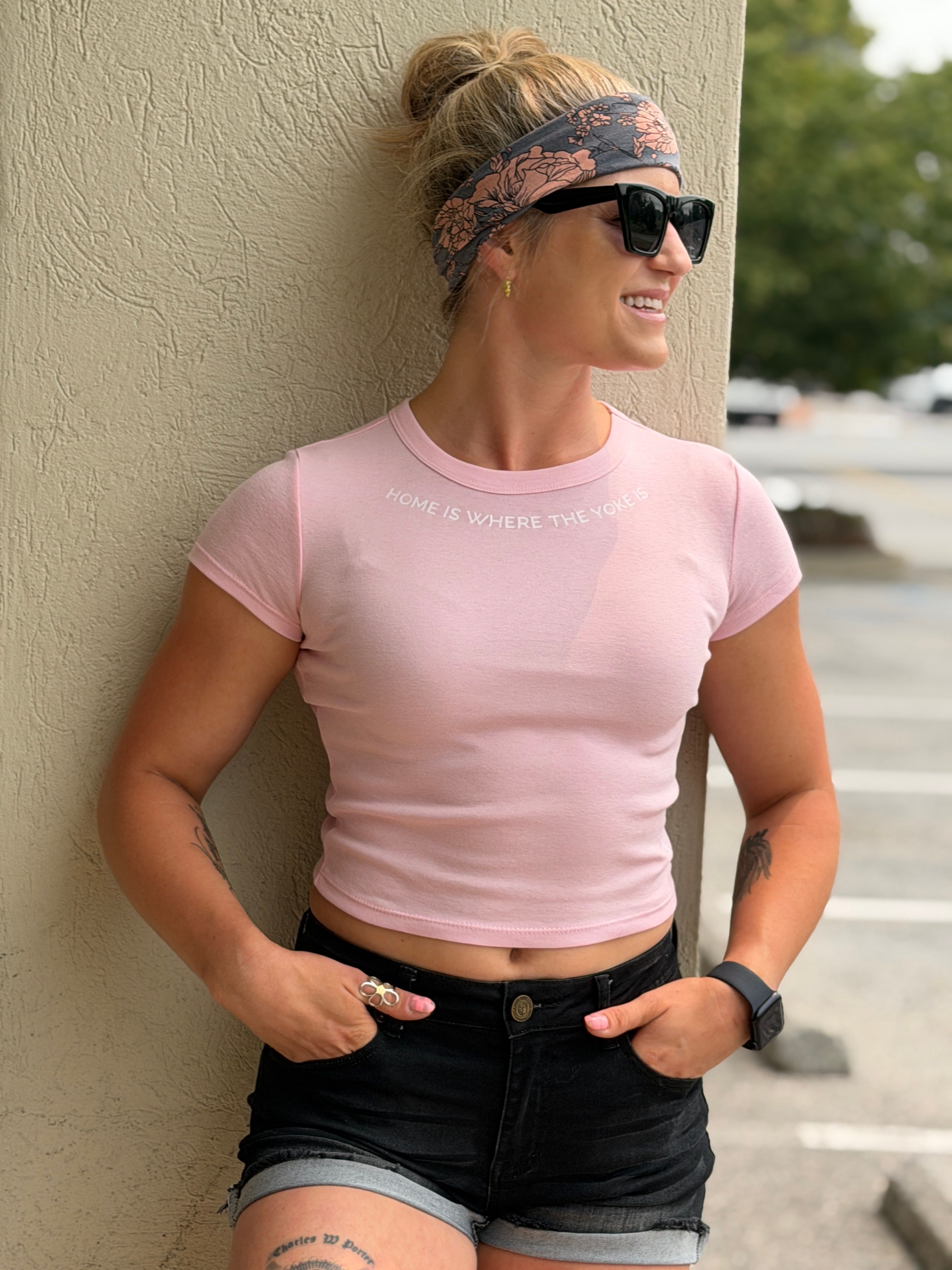 Sam Fox leaning against a wall in the pink cropped baby tee printed with “Home is where the yoke is”.
