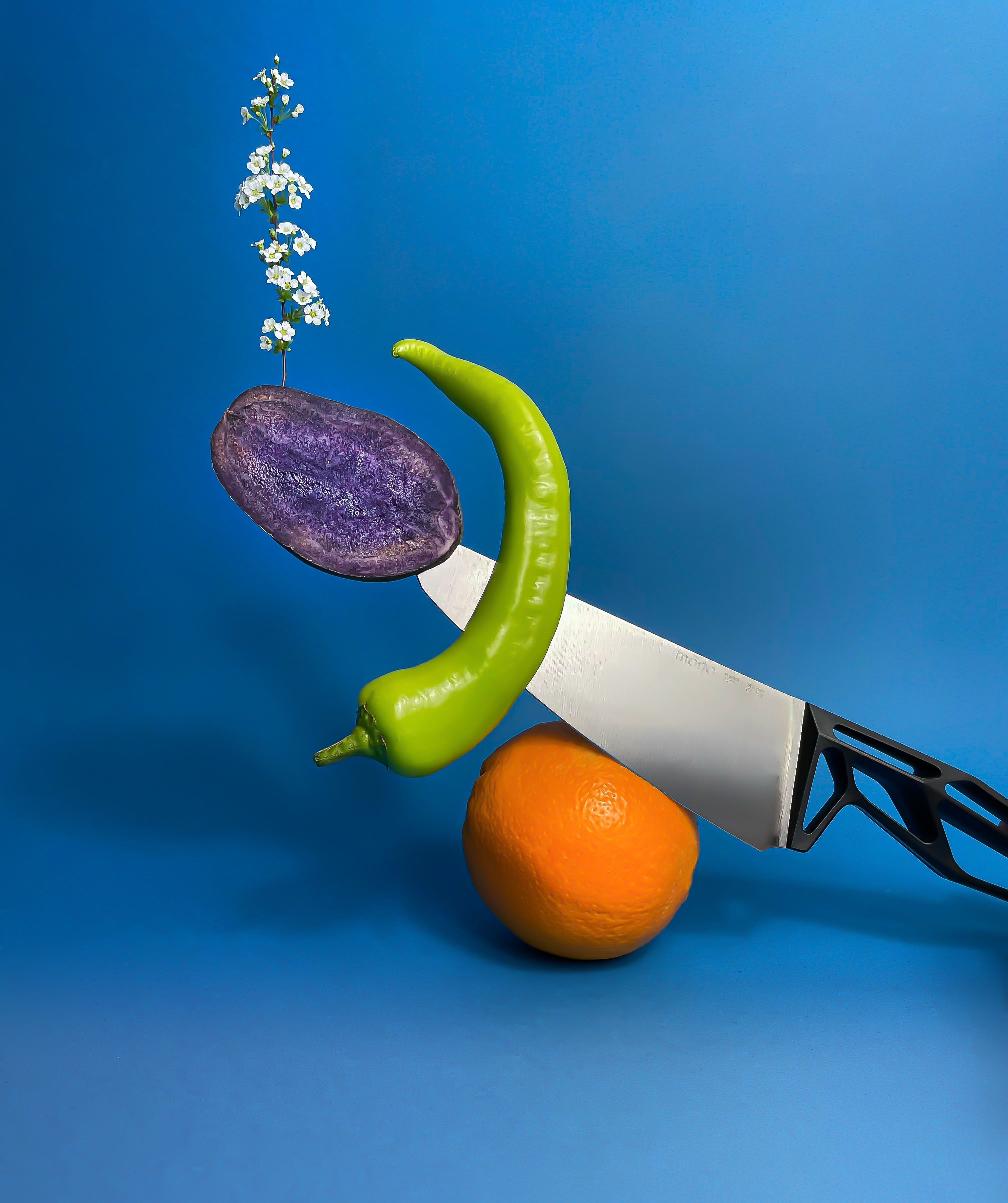 Knife impaling a blue potatoe, pepper and blossoms leaning on an orange