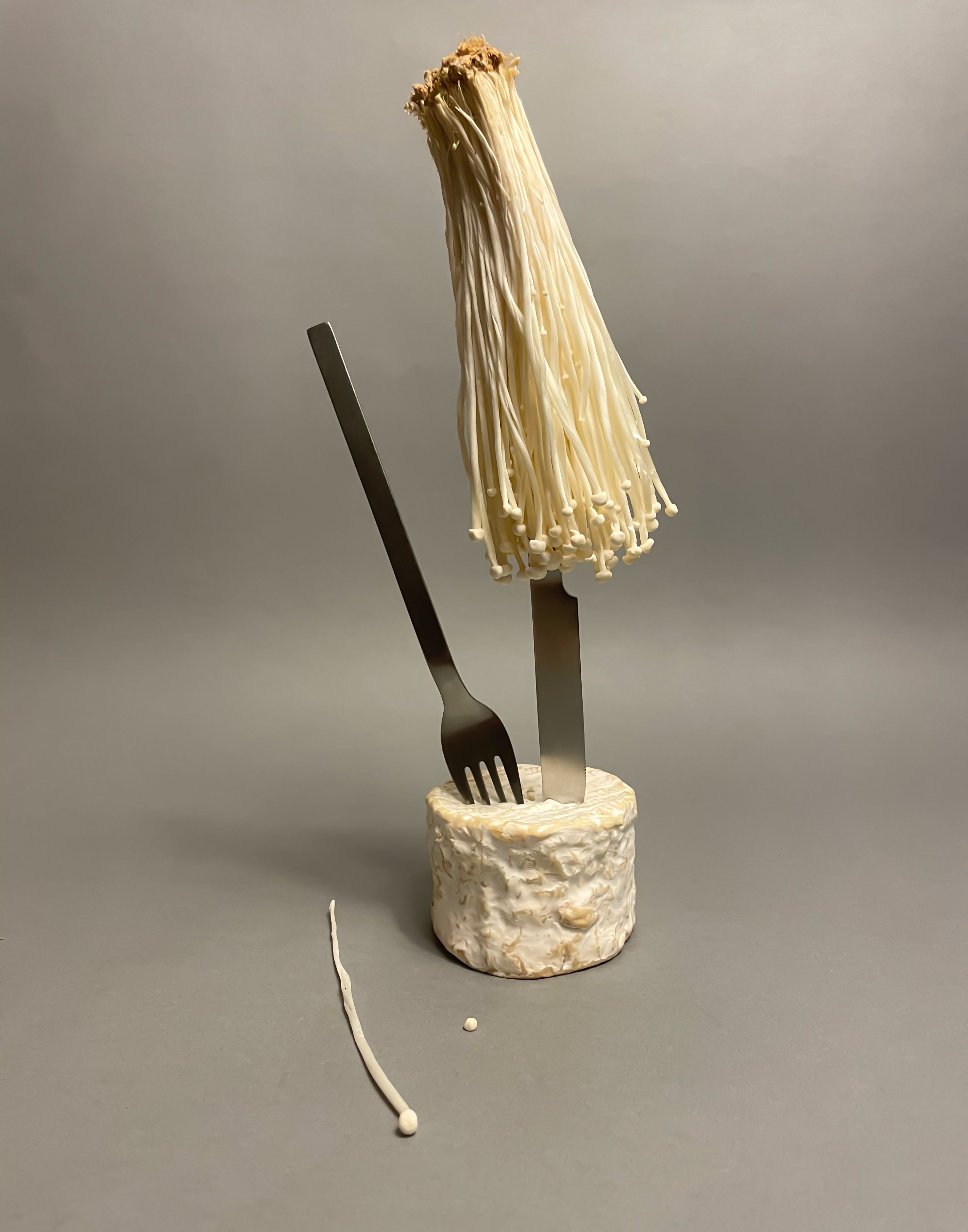 Arrangement of a fork and knife with an enoki mushroom and goat cheese