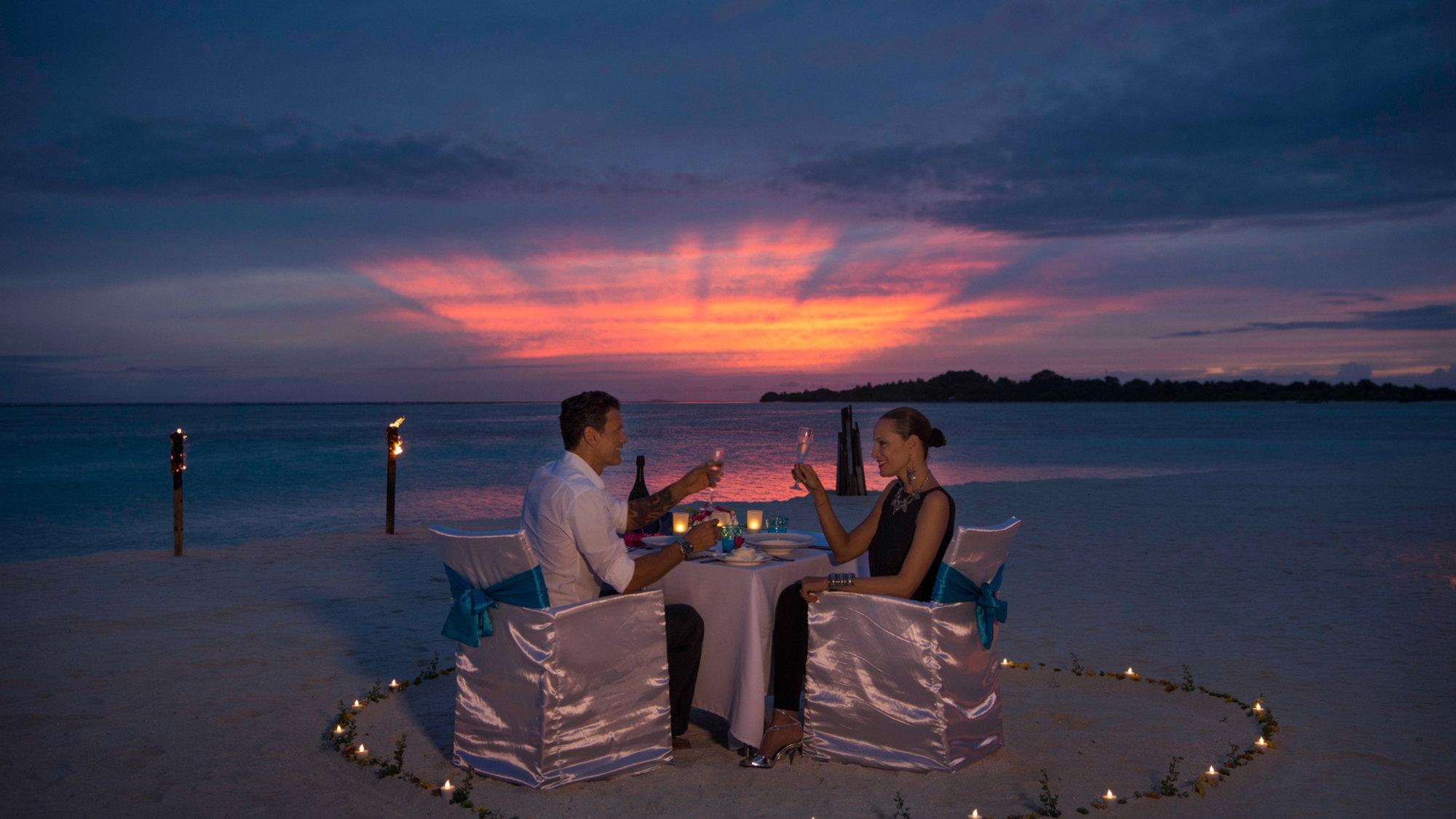 Couple dining on the beach at sunset in the Maldives