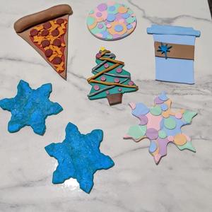 a variety of clay shapes, like 2 blue snowflakes, a snowflake and a circle with pastel colored overlapping circles, a slice of pizza, a christmas tree, and a blue starbucks-style coffee cup