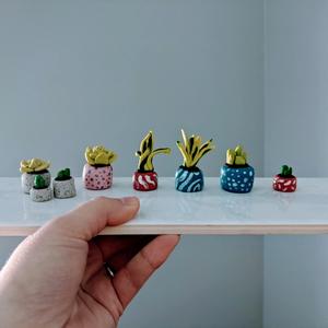 a hand holding a ceramic tile with a variety of mini succulent figurines on it