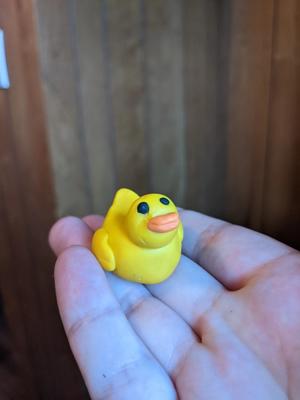 a hand holding a small yellow polymer clay duck (like a rubber duck)