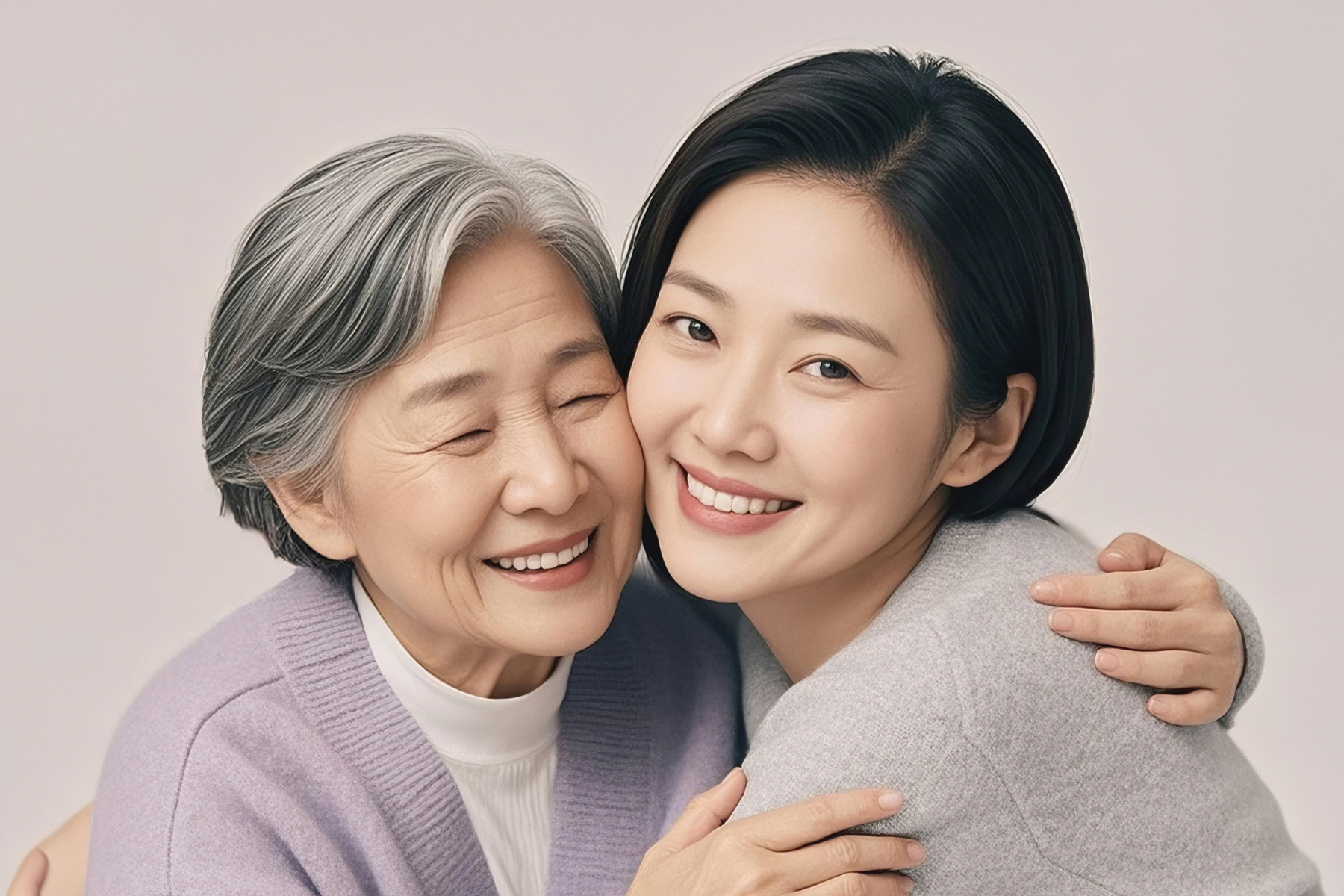 An older woman and a younger woman leaning their heads together, both with eyes closed.