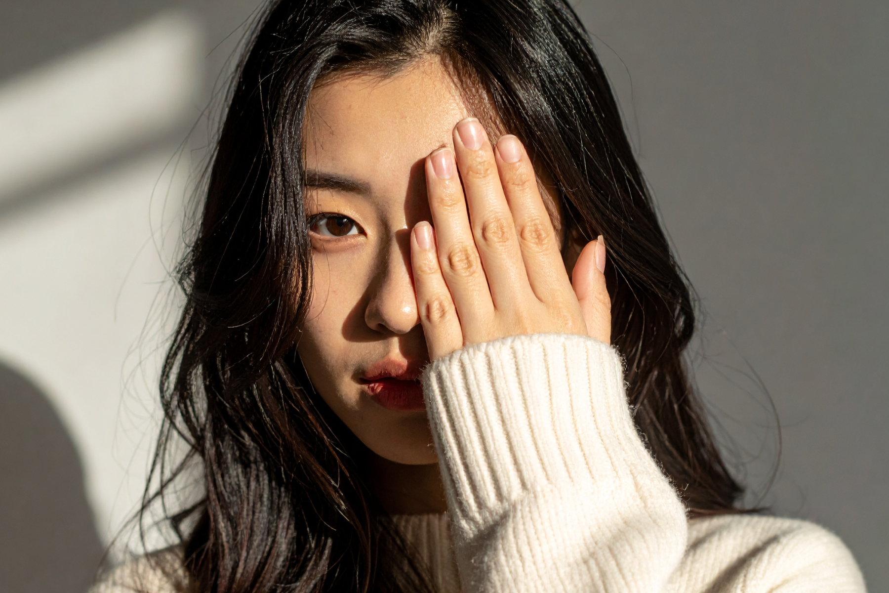 A woman covering one eye with her open hand, the other eye looking toward the camera in daylight.