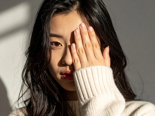 A woman covering one eye with her open hand, the other eye looking toward the camera in daylight.