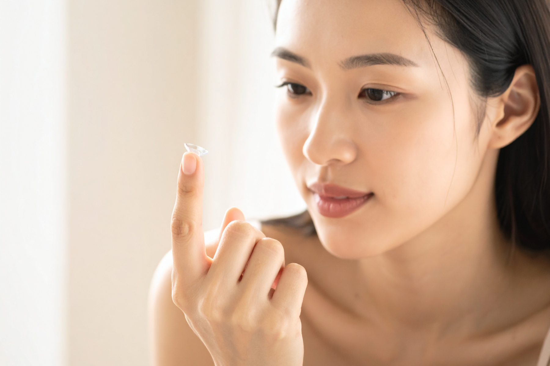 A woman holding a contact lens on her fingertip and looking at it.