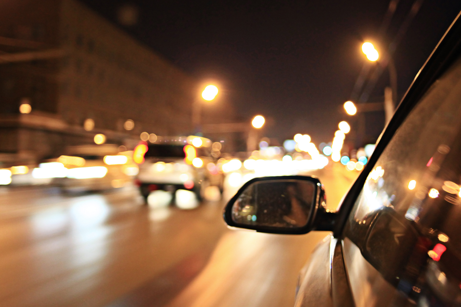 Street lights and car headlights at night appearing as soft glowing halos, seen from a moving vehicle.