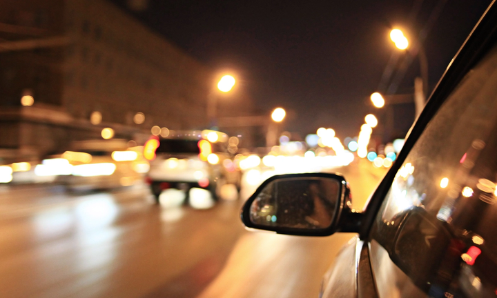 Street lights and car headlights at night appearing as soft glowing halos, seen from a moving vehicle.