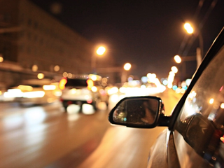 Street lights and car headlights at night appearing as soft glowing halos, seen from a moving vehicle.