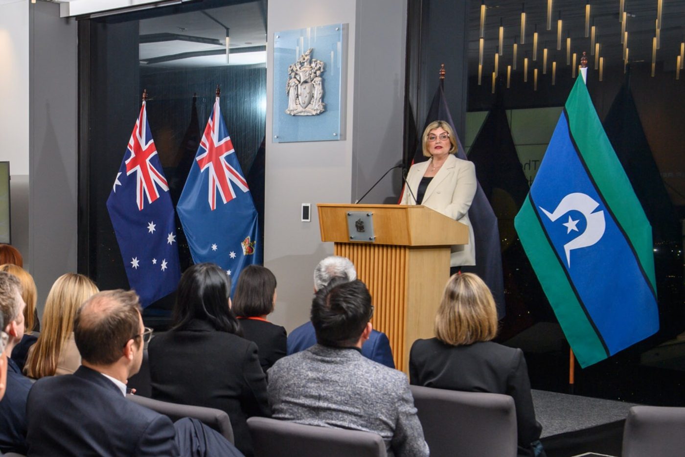 Natalie Suleyman speaking at a lectern in front of the Australian, Victorian and Torres Strait Islander flags