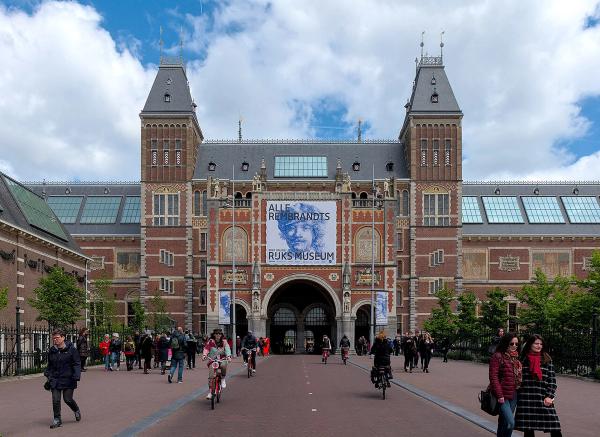 Façade en brique rouge du Rijksmuseum d'Amsterdam avec ses deux tours, des cyclistes et visiteurs passant sous le passage central - Credit:Wikipedia