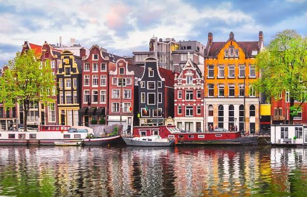 Maisons de canal colorées et penchées d'Amsterdam se reflétant dans l'eau, avec des péniches amarrées le long du quai