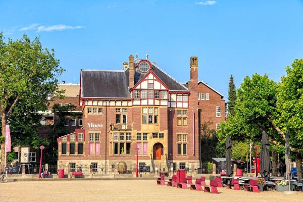 Façade en brique rouge de la Villa Alsberg abritant le Musée Moco sur la Museumplein à Amsterdam, avec les bancs rouges de la place