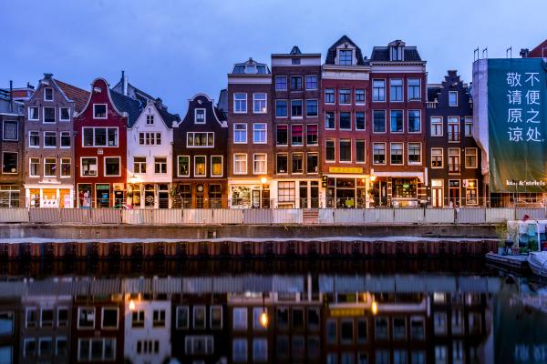 Rangée de maisons de canal colorées d'Amsterdam avec leurs pignons typiques, illuminées et reflétées dans l'eau du canal au crépuscule. © Pexels