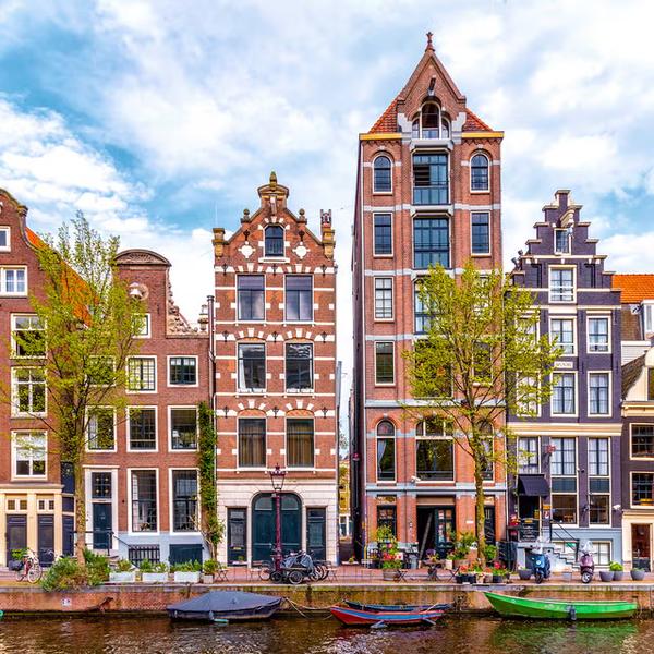 Maisons de canal à pignons du XVIIe siècle le long d'un canal d'Amsterdam, avec des barques amarrées et des vélos sur le quai © Cosmopolitan