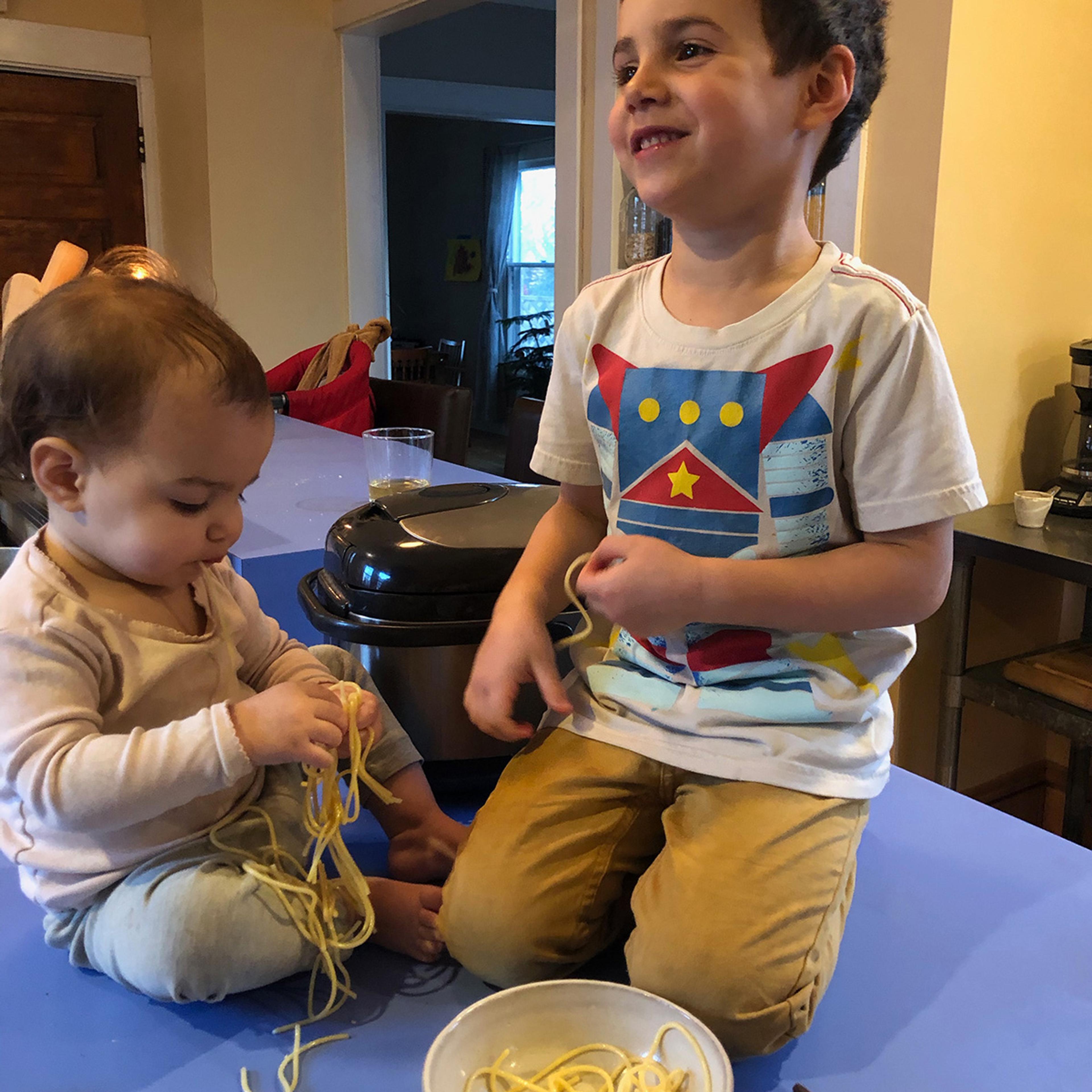Kid sitting on counter eating pasta. Photo by The Perennial Plate.