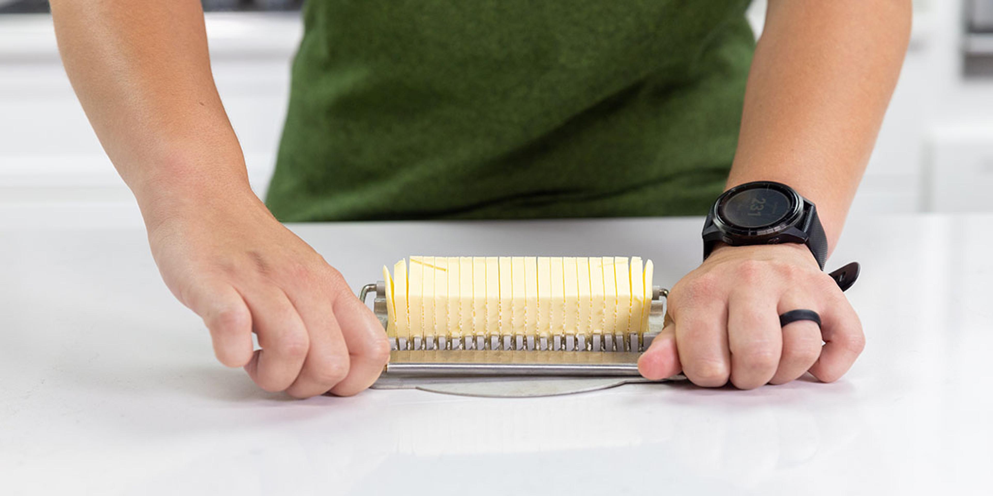 A woman pushes down the arm of a stainless steel butter cutter and chops butter into about 20 pieces.