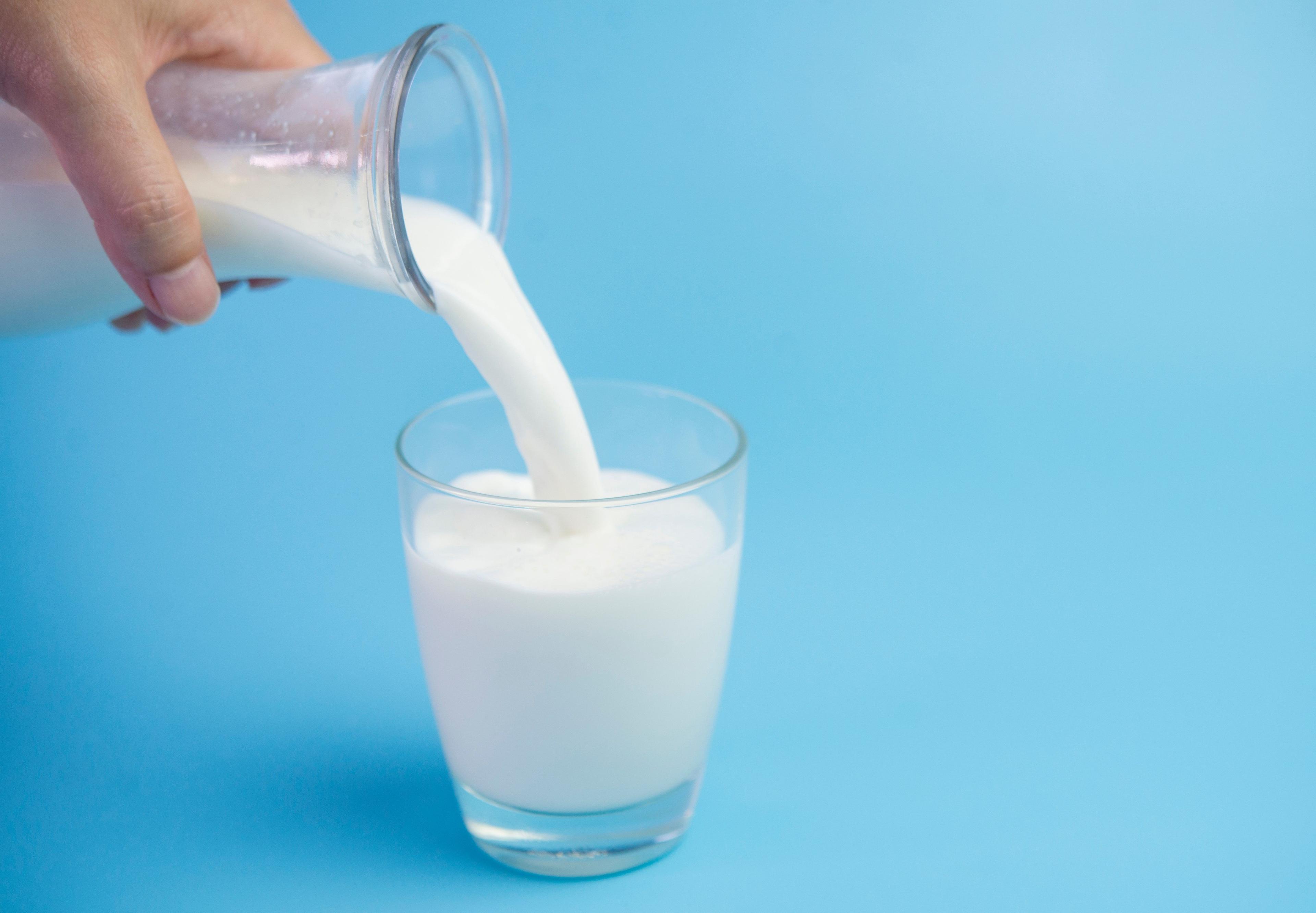 A person pours milk into a glass from a carafe.