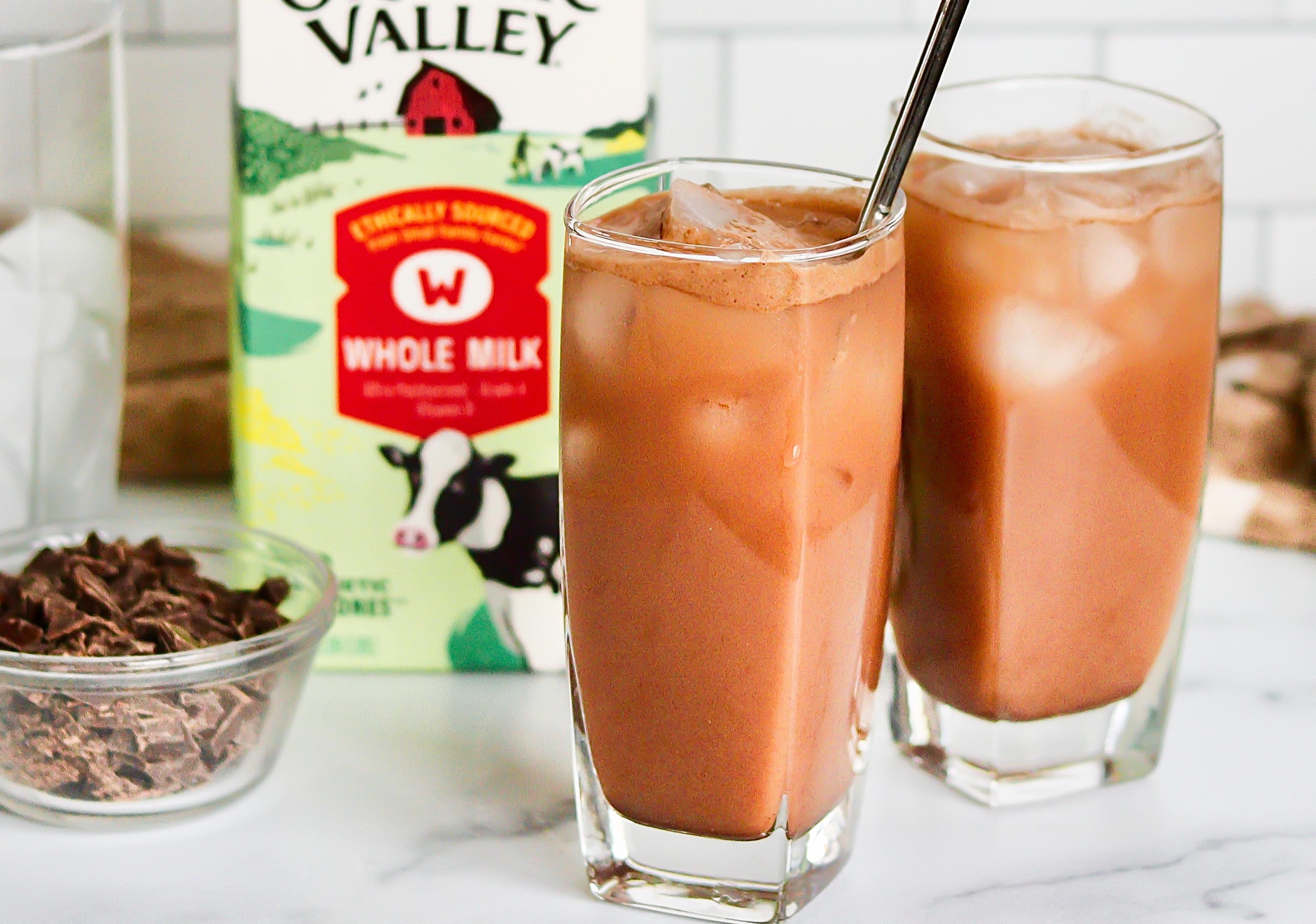 Two glasses of iced hot chocolate on a counter with organic whole milk and chocolate pieces.