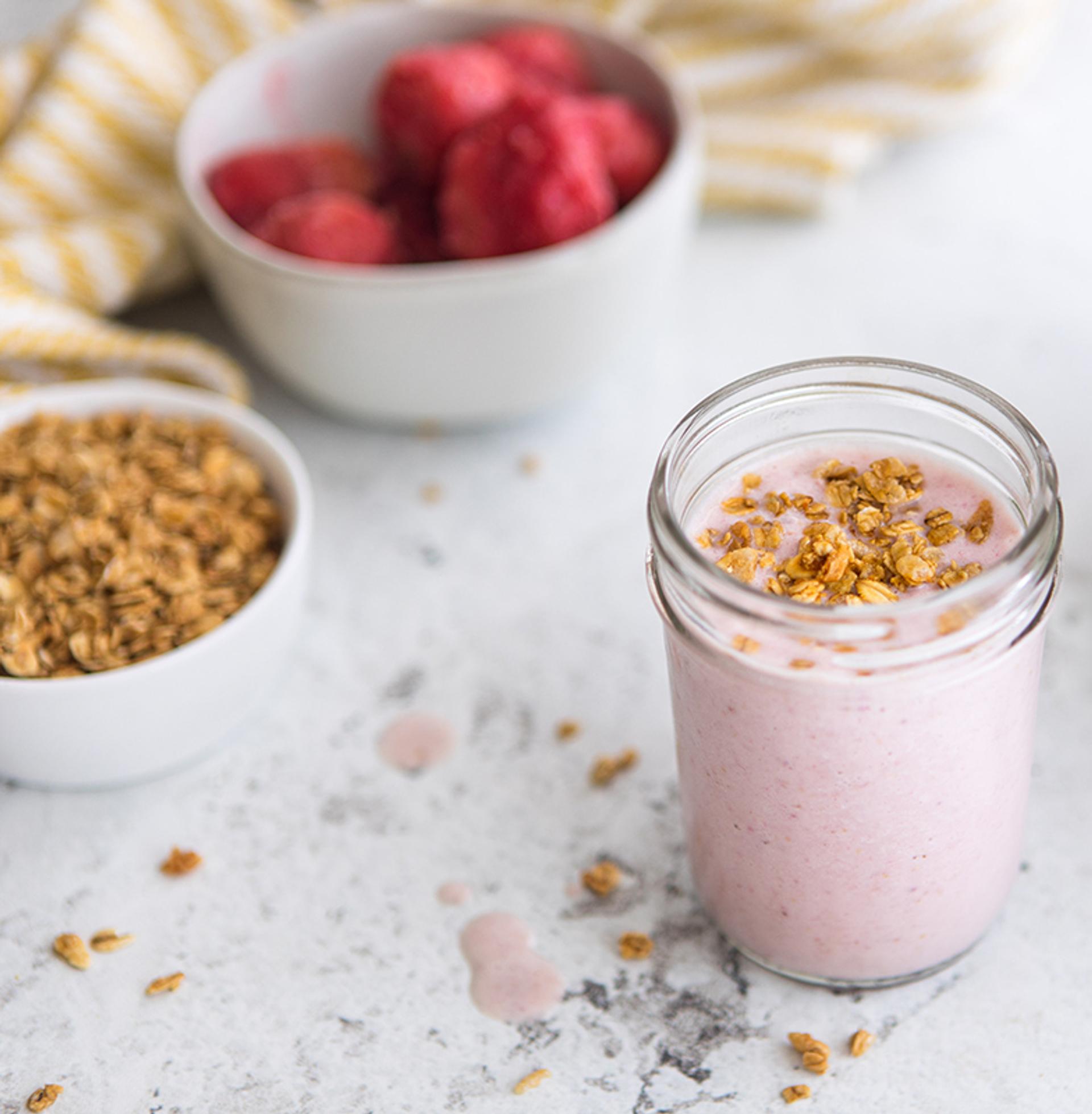 Strawberry Banana smoothie topped with granola sits on a marble countertop with Organic Valley milk and granola.