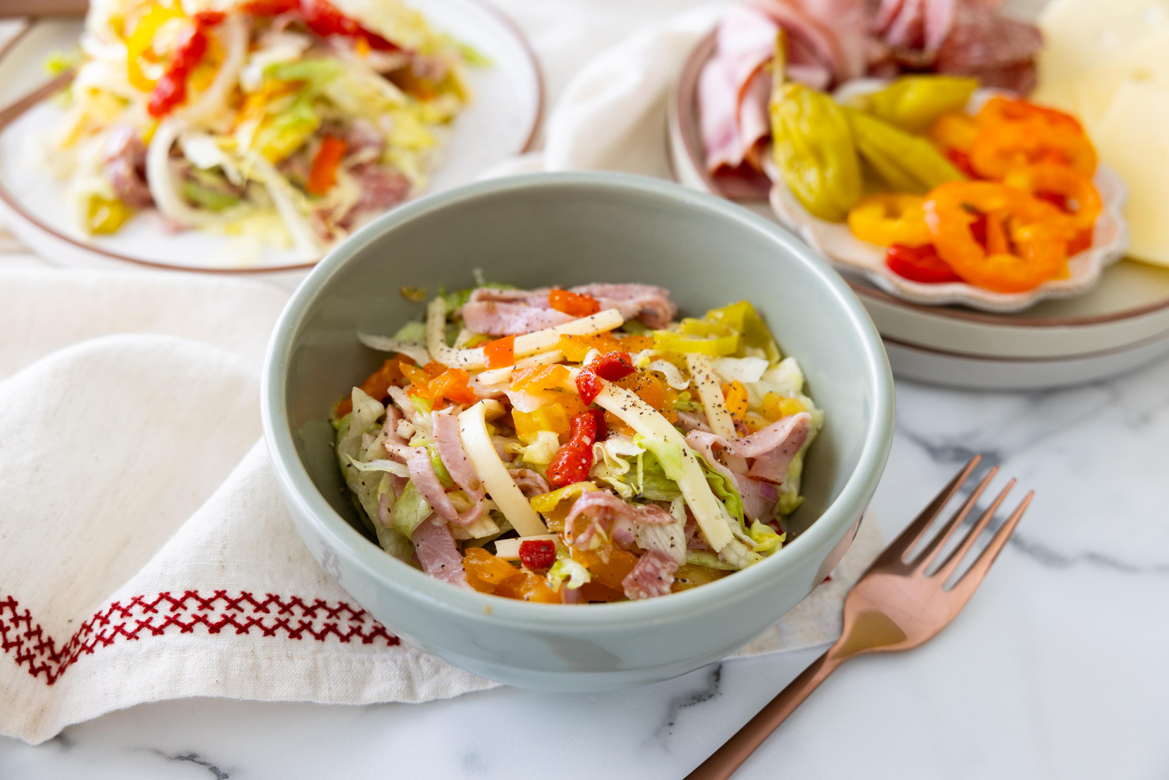 A grinder salad in a bowl includes Swiss cheese and deli slices.