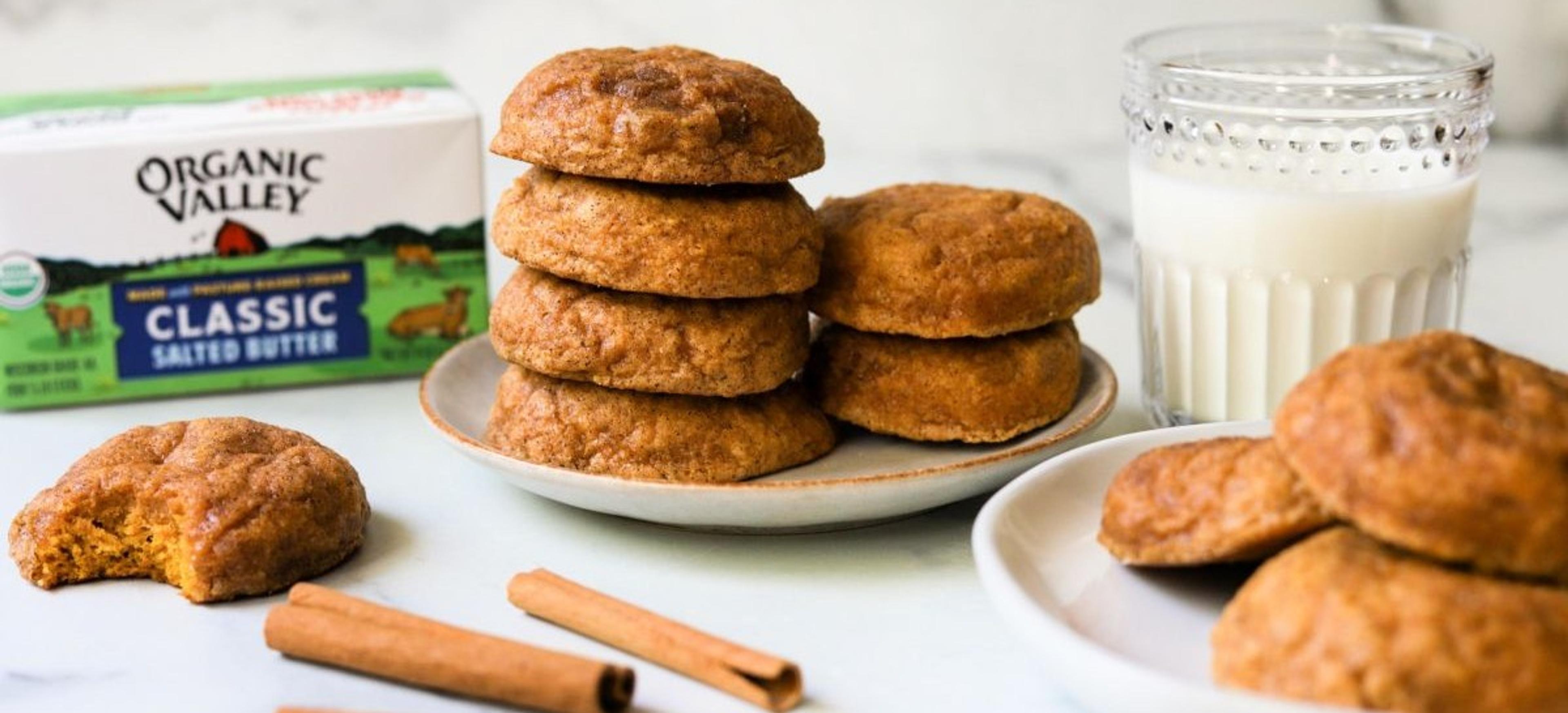 Pumpkin spice cookies on a plate next to milk, cinnamon sticks and salted organic butter. 