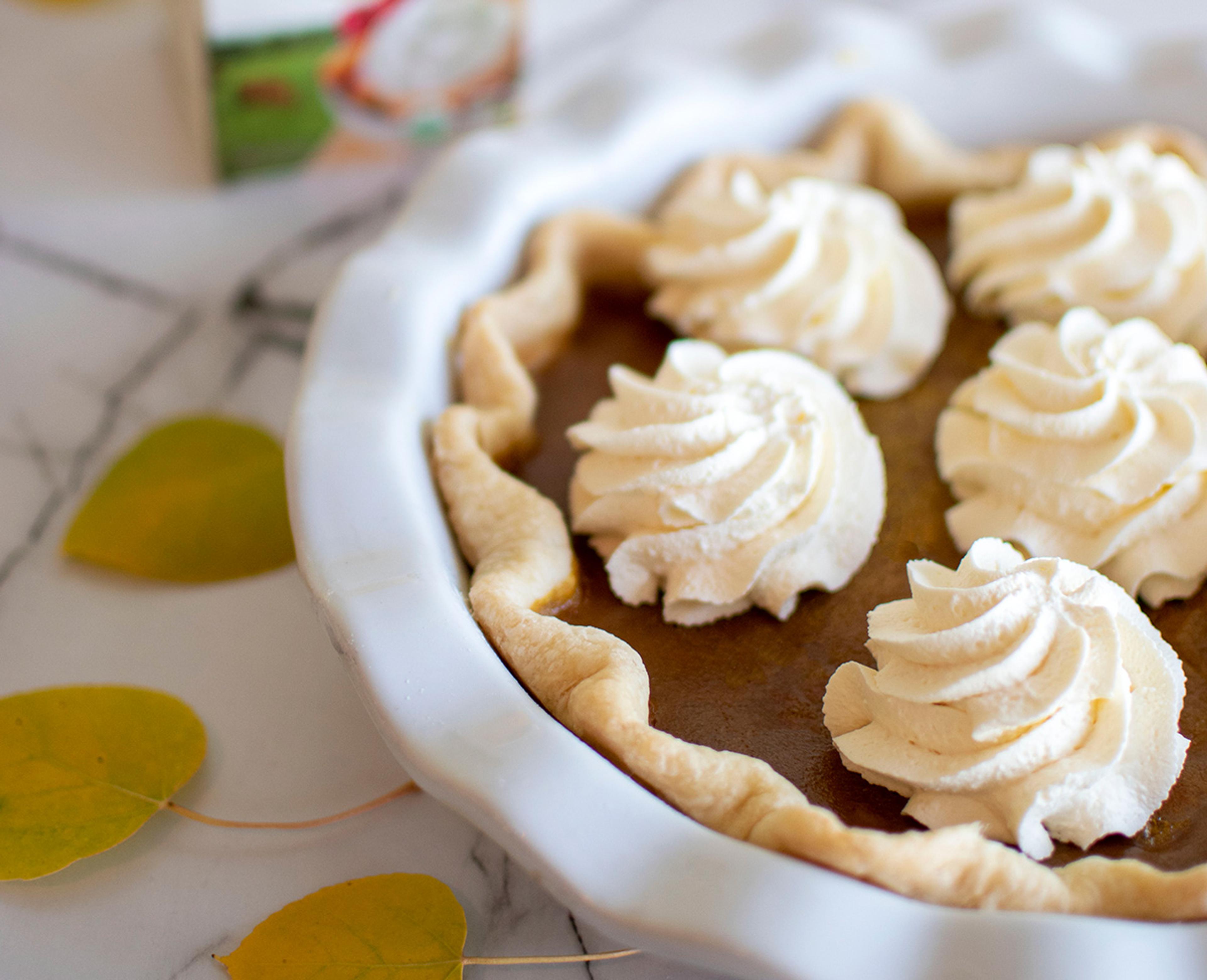 A close up of pumpkin pie with florets of whipped cream on top, surrounded by yellow fall leaves.