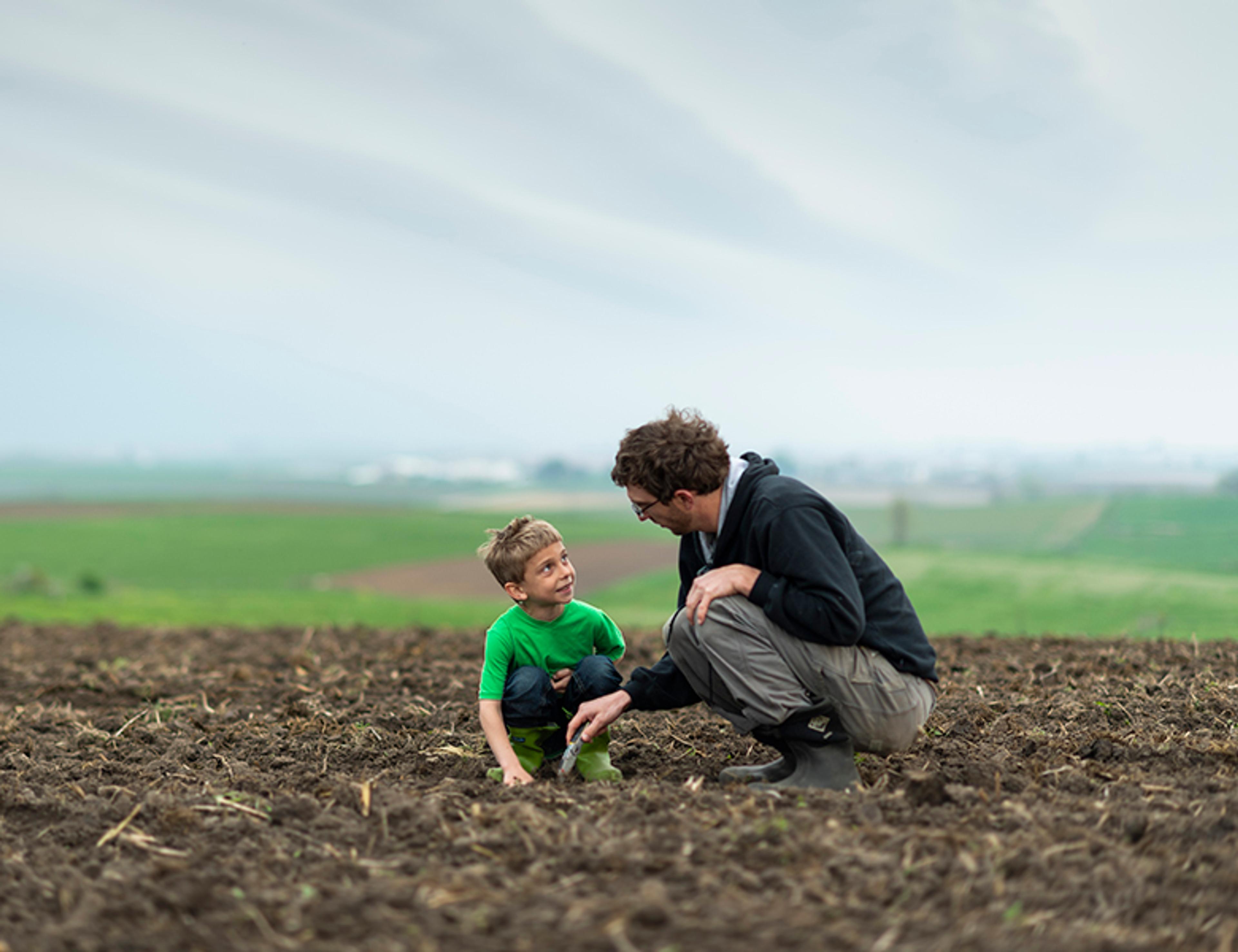 Farmer talks to young son in a freshly tilled field. 