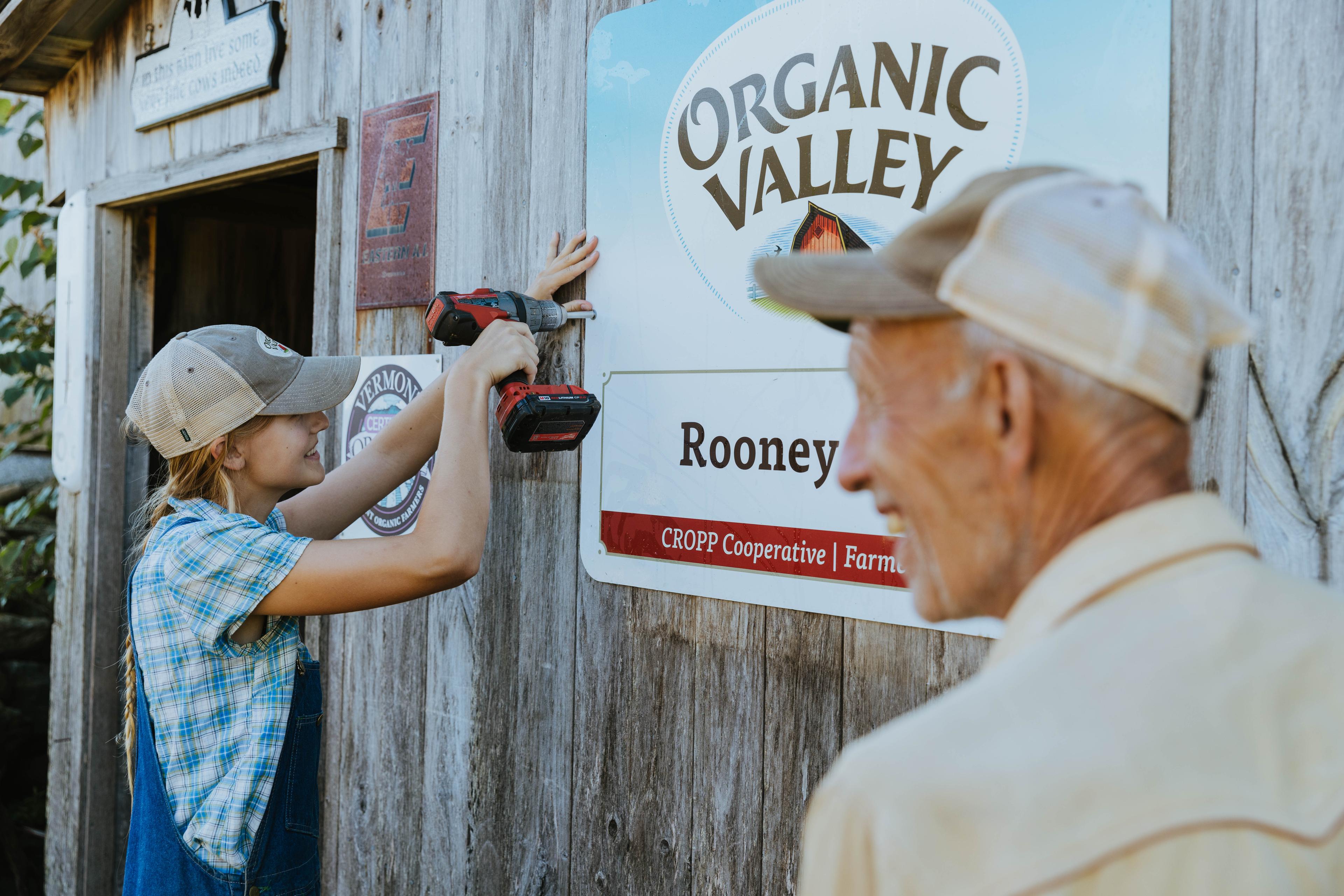 A woman screws an Organic Valley sign onto a barn while a family member looks on.