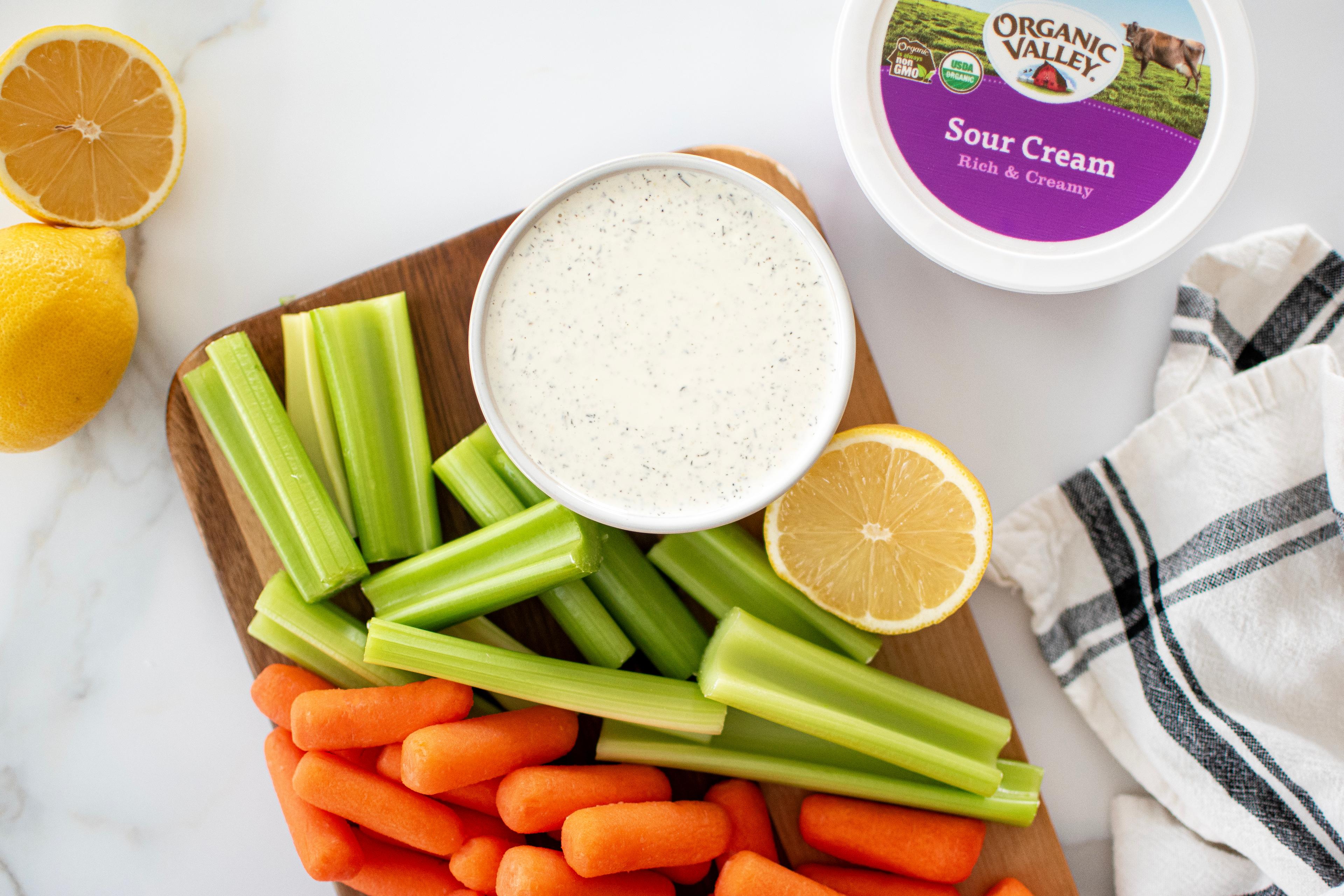 Garlic Lemon Dill Dip displayed on a cutting board with lemon, carrots and celery.