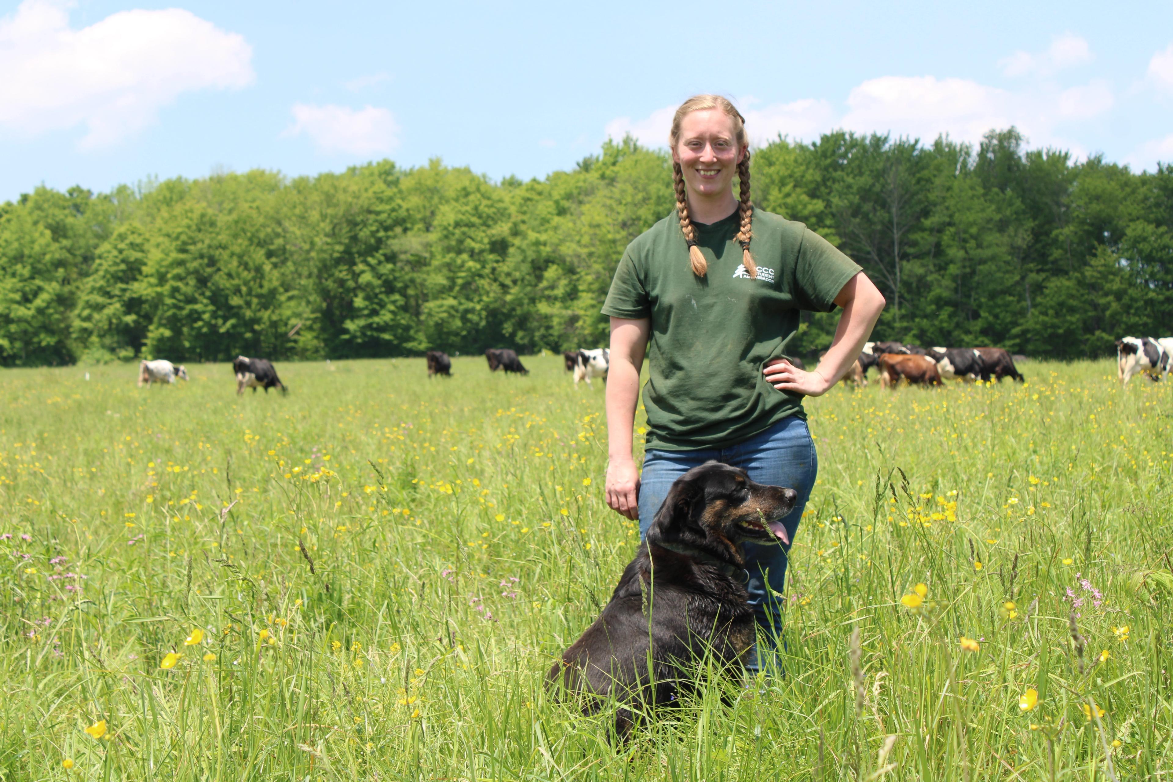 Melissa Moody and a dog in a field with cows grazing in the background.