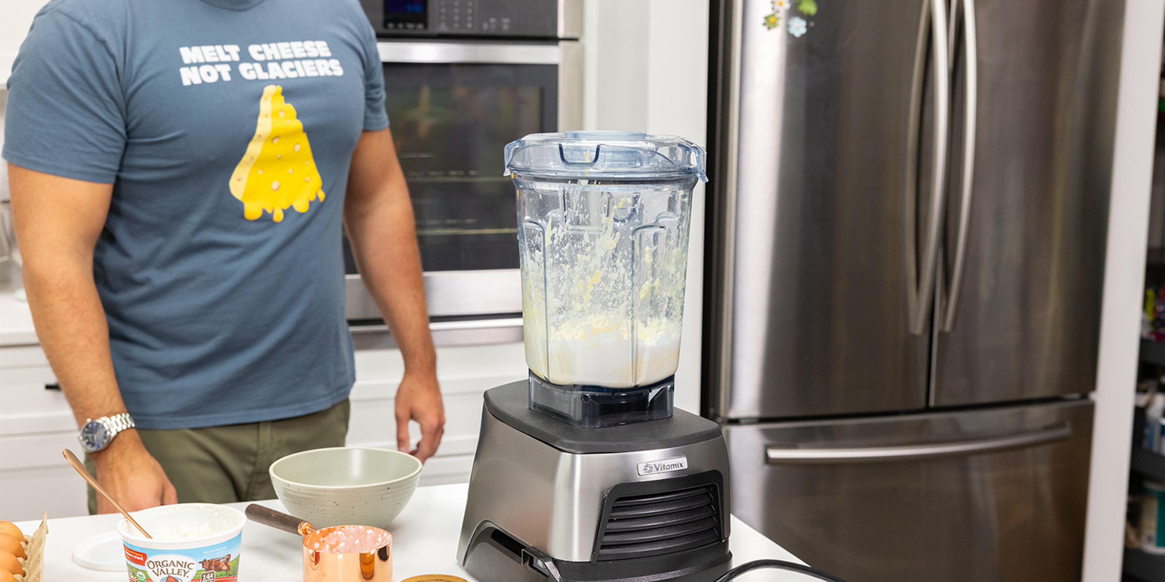 A man stands by a blender that has cottage cheese and an egg in it.