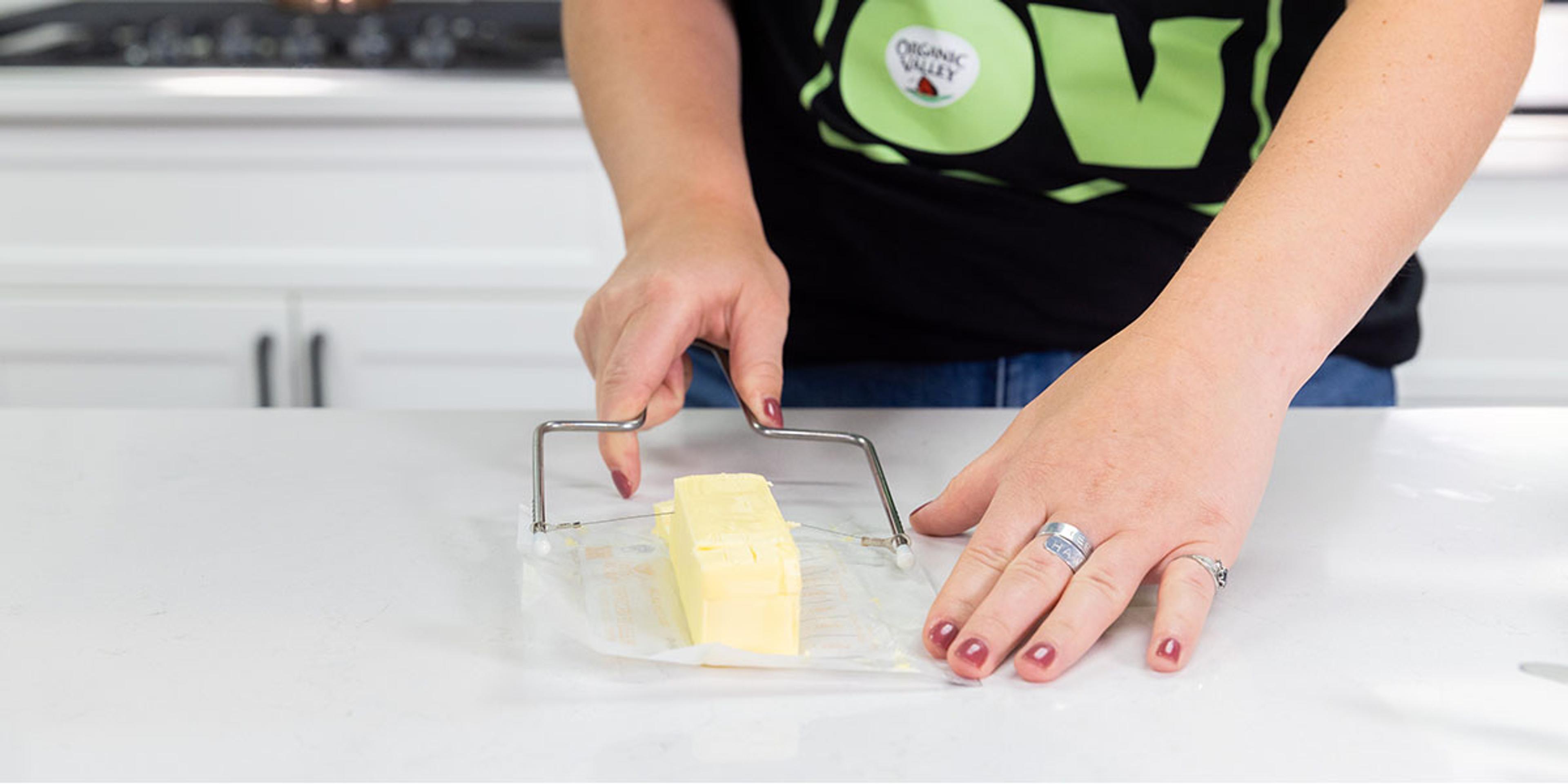 A woman wearing an Organic Valley T-shirt slices butter with a wire butter cutter.
