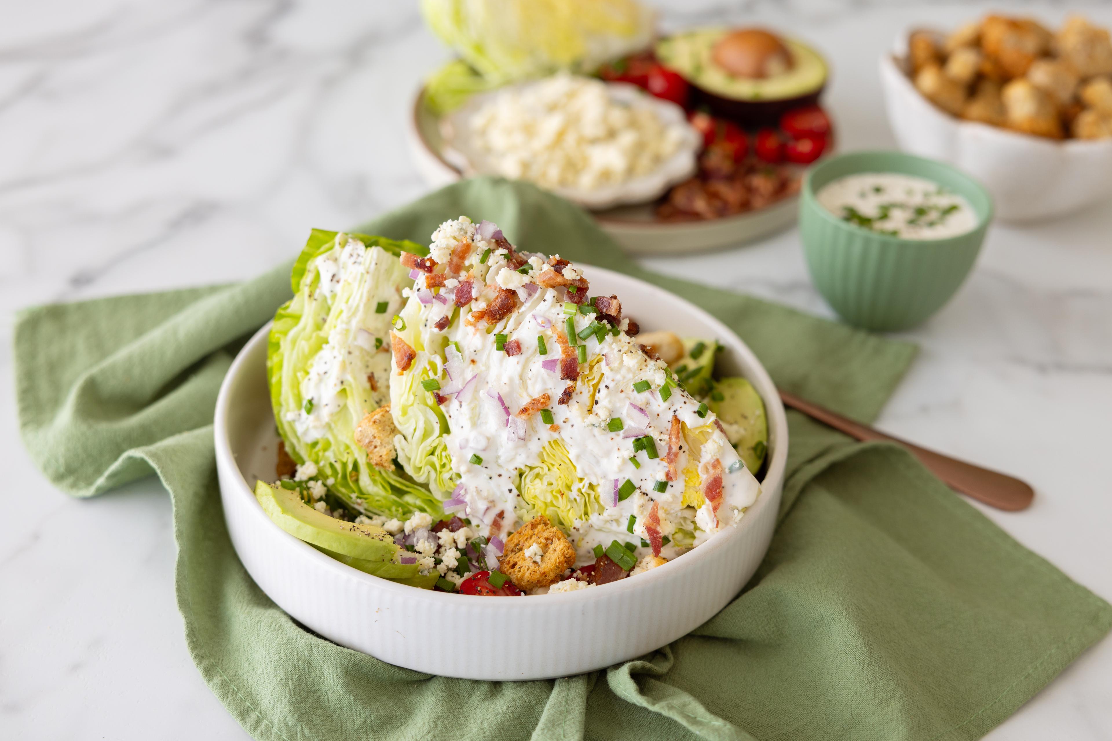 A wedge salad with bacon, onion and blue cheese dressing on a table.