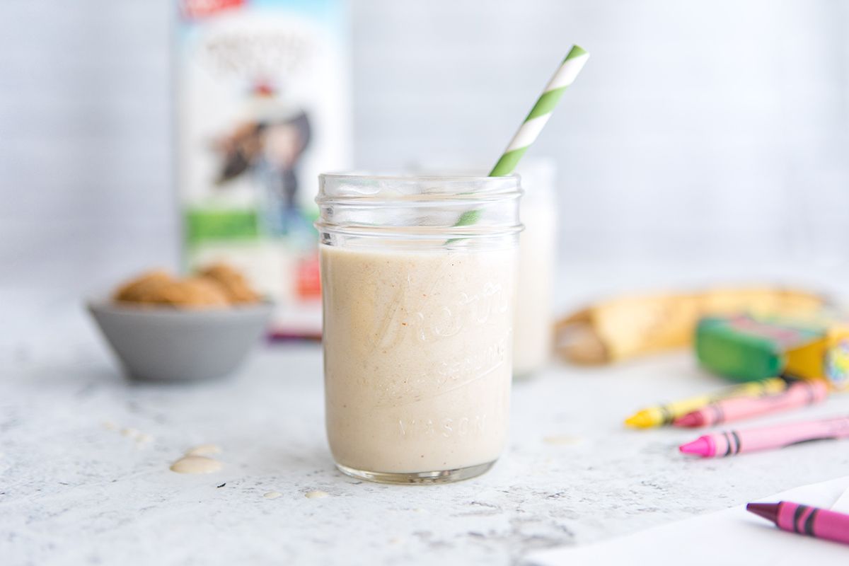 Side view of a light-colored smoothie in a mason jar with a striped green and white straw, and crayons scattered around.