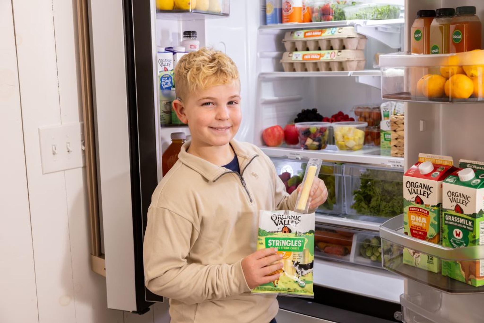 A boy holds a Stringles string cheese in front of a stocked refrigerator.