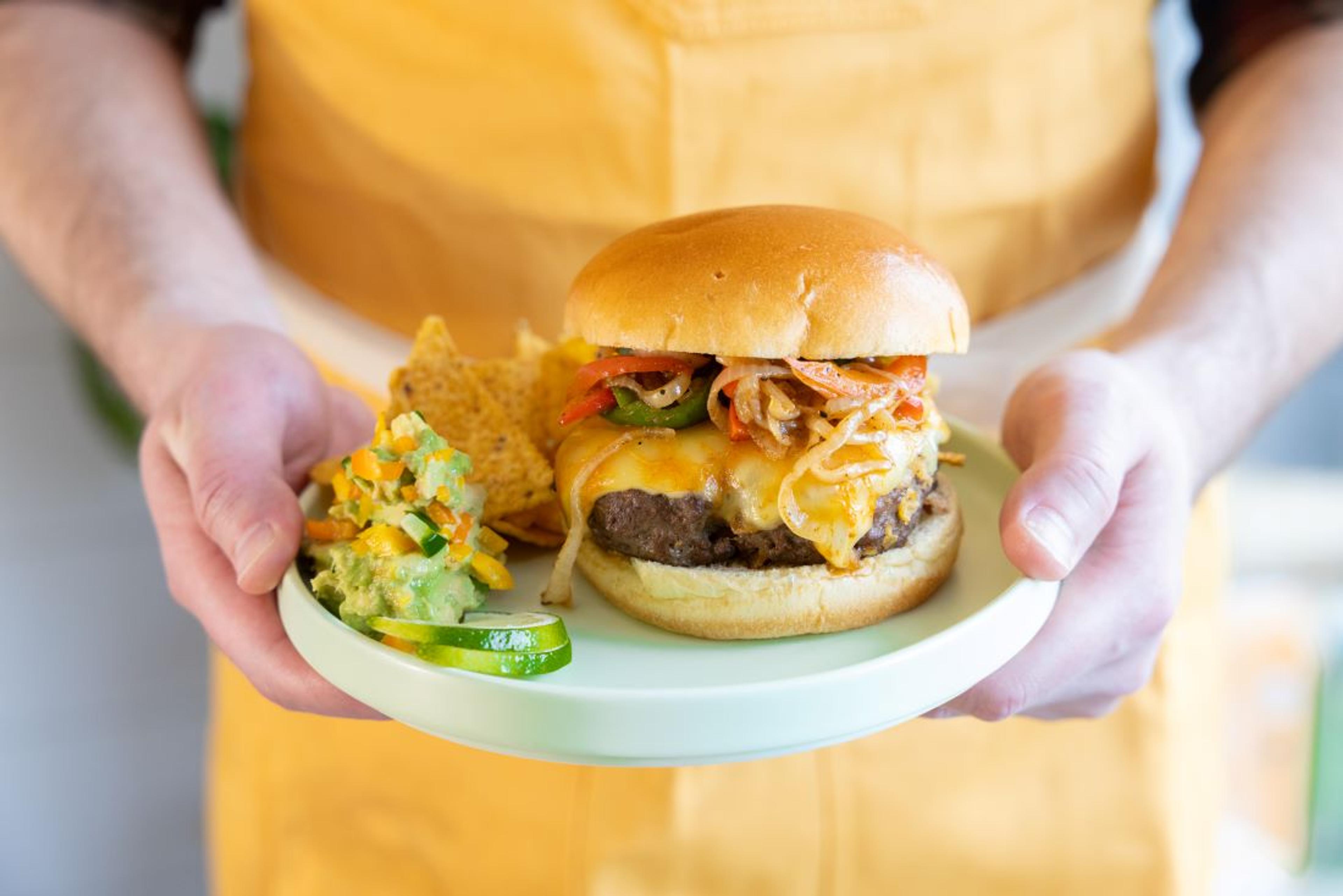 A person holds a plate with a cheeseburger and chips on it.