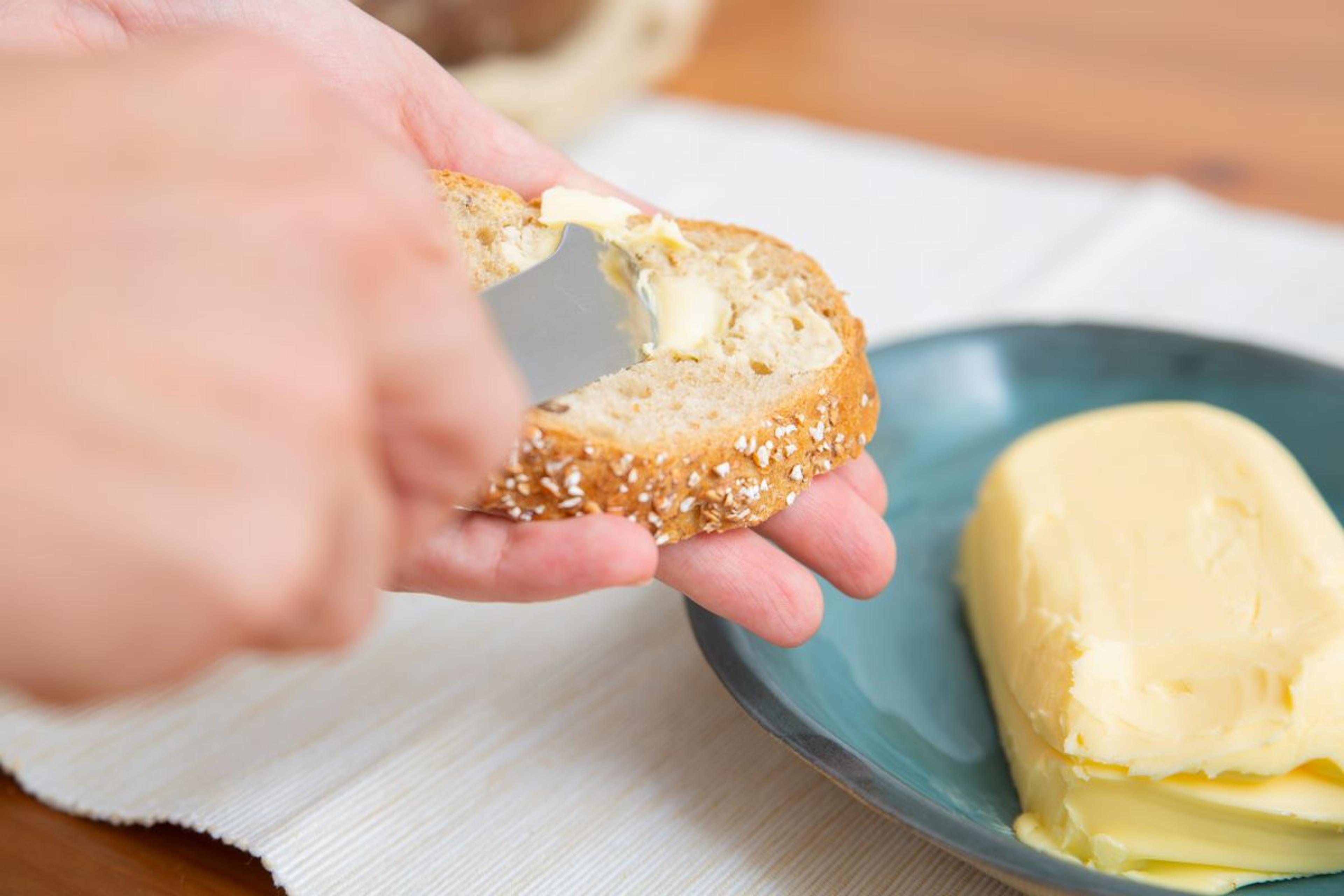 A person spreads butter on a whole grain baguette.