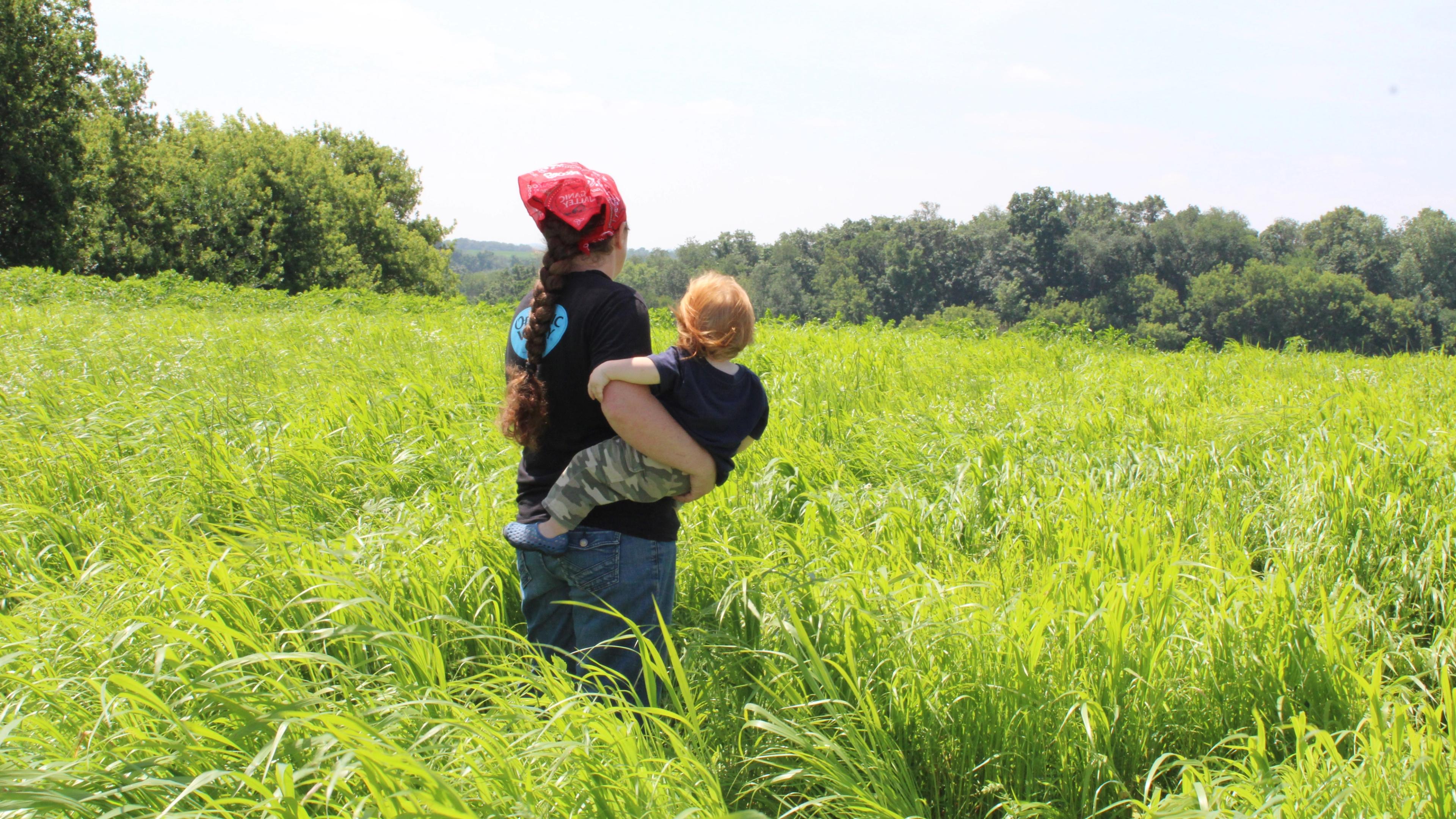 A mom holds her baby in a field of grass. 