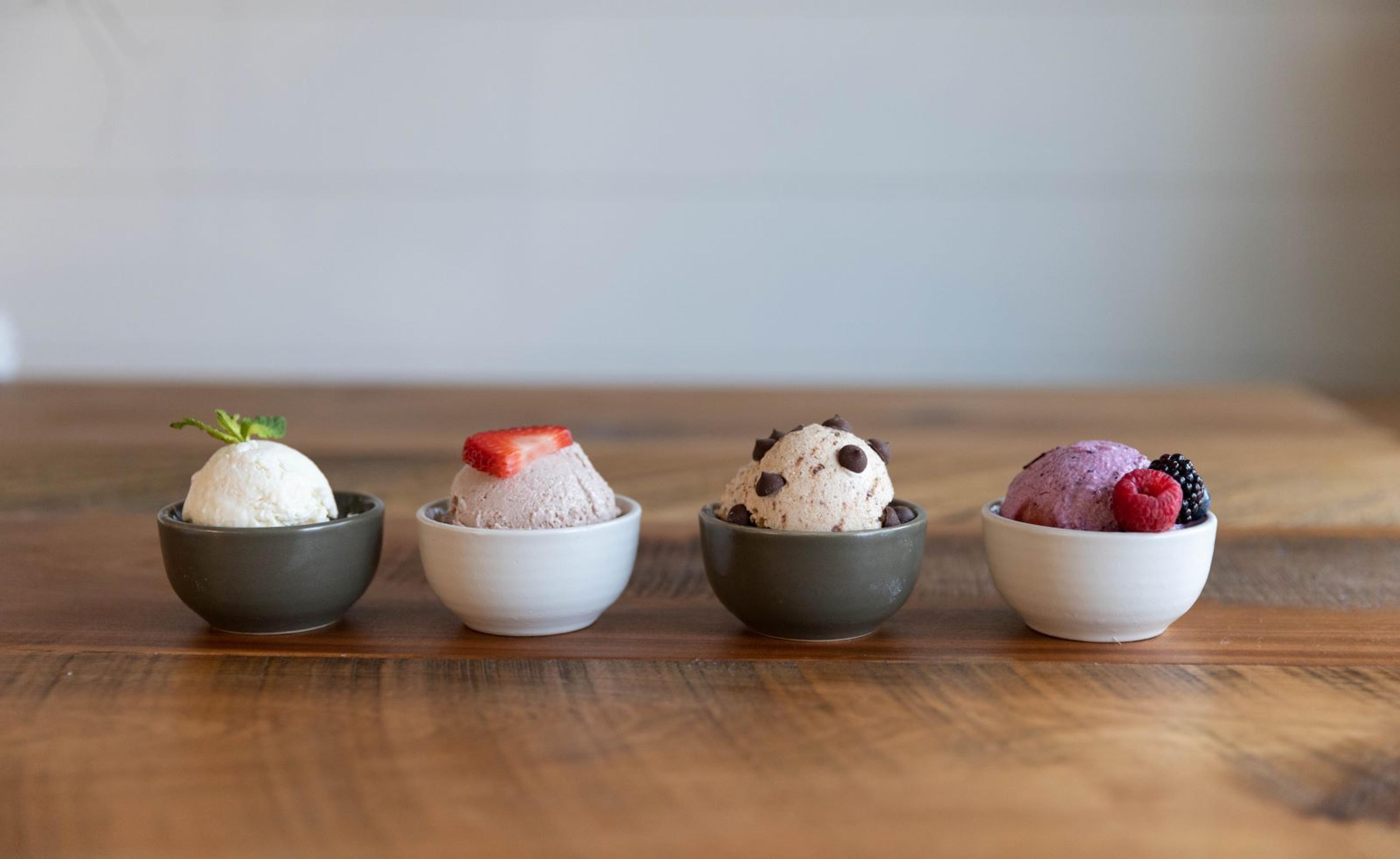 4 bowls of ice cream with varying toppings on a wooden table.