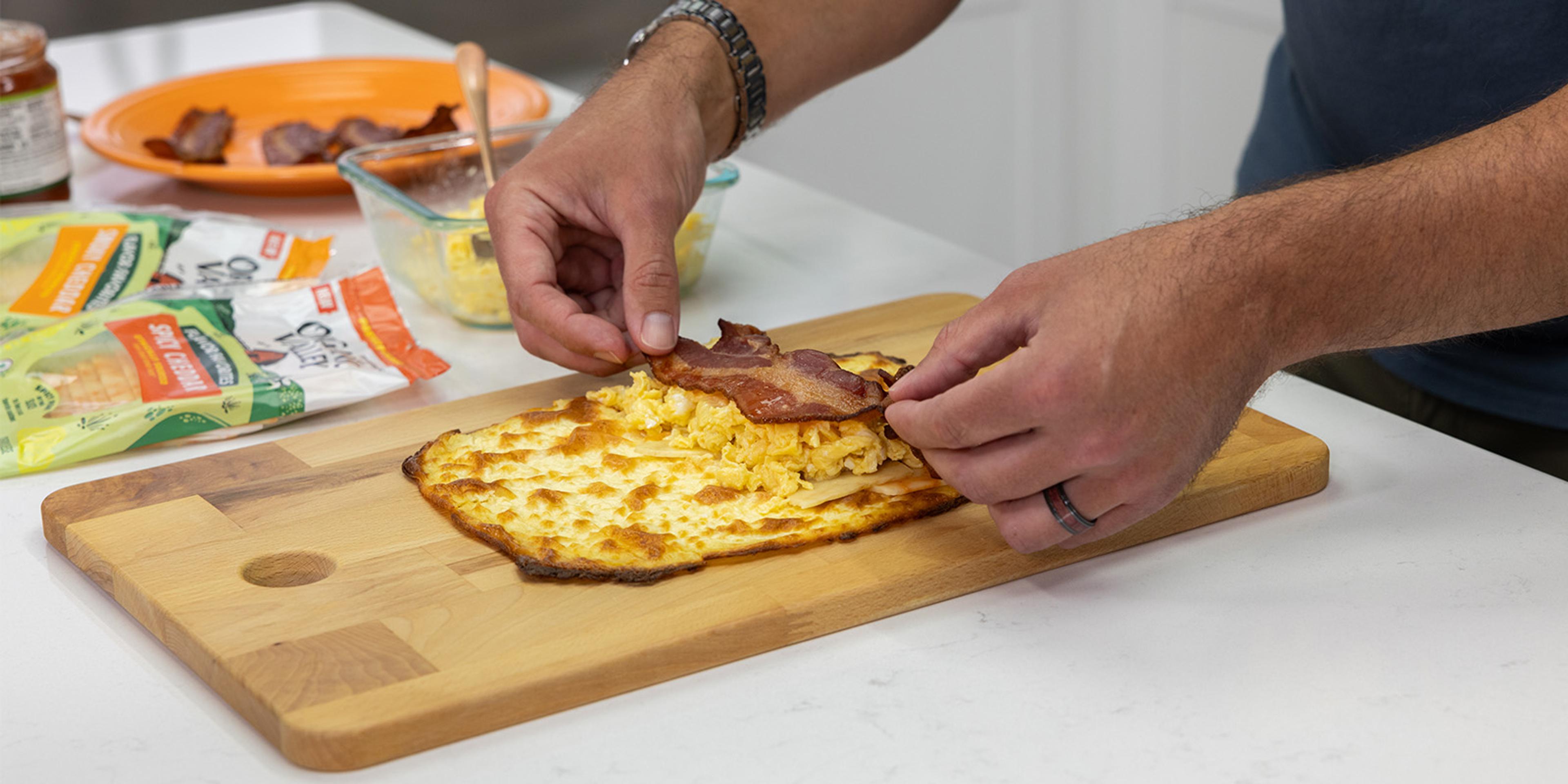 A man puts bacon and scrambled eggs on cottage cheese bread.